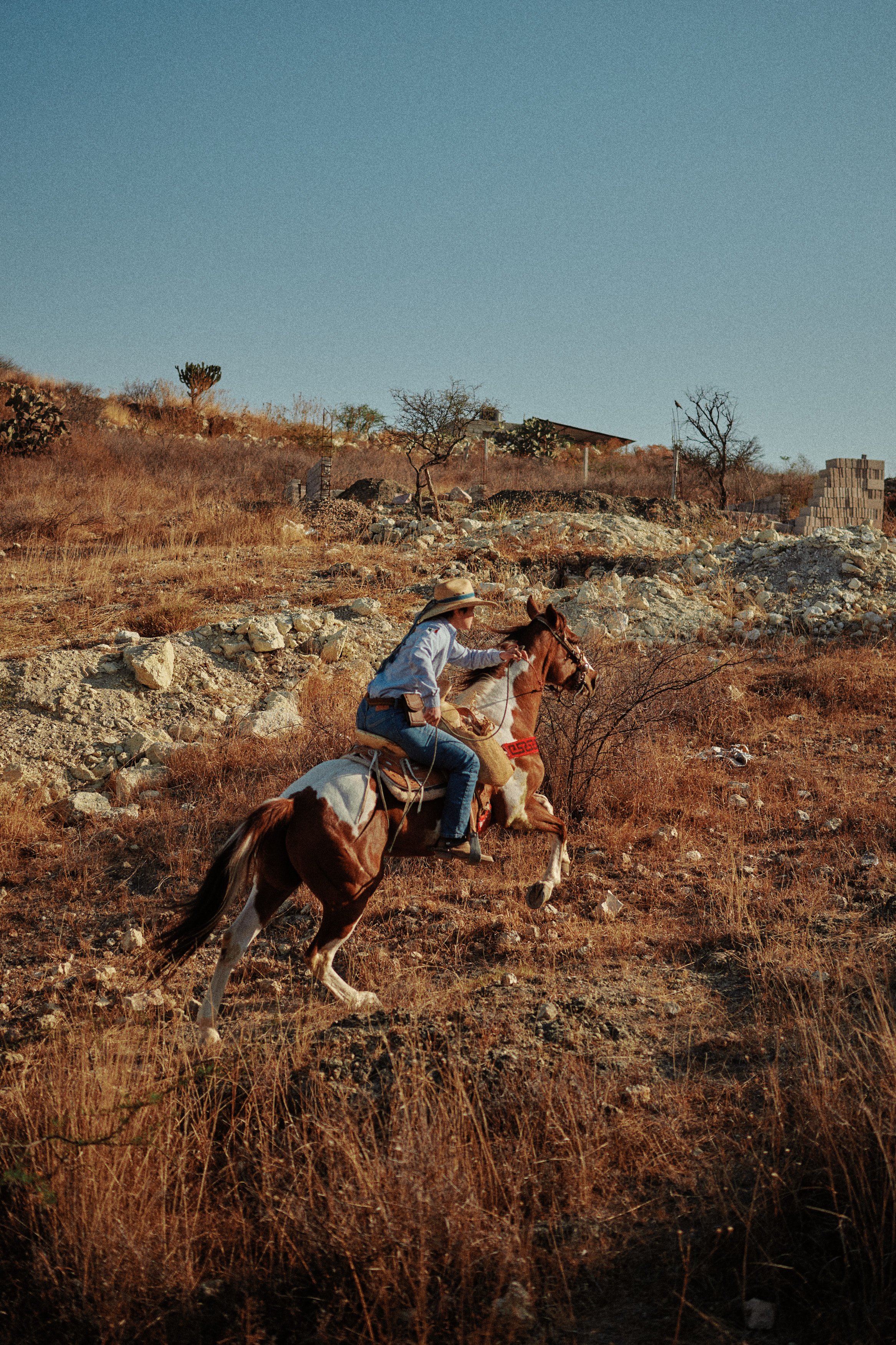 A person riding a horse up a dry, rocky hill under a clear blue sky.