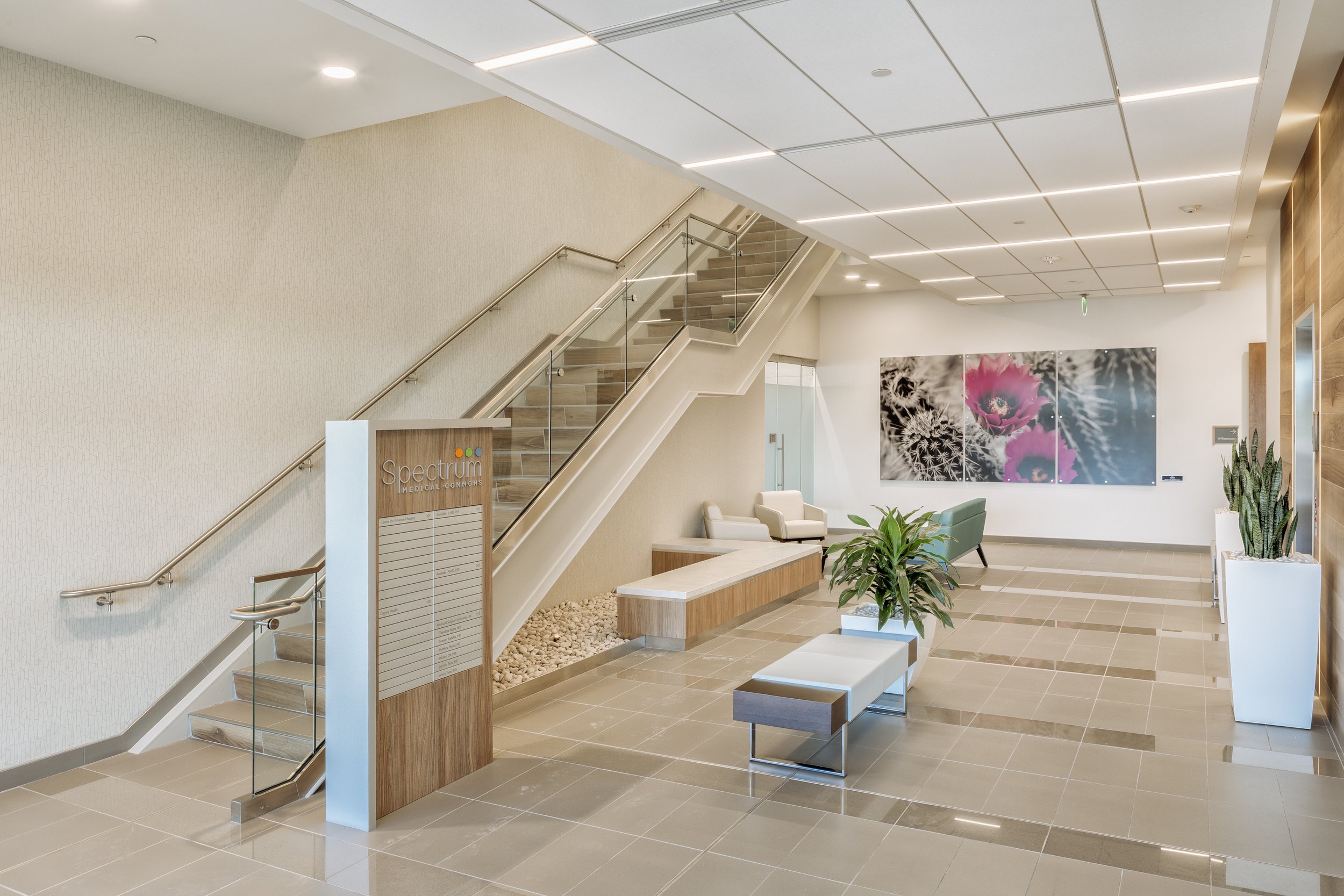 Modern medical office reception area with seating, plants, wall art, and a staircase.