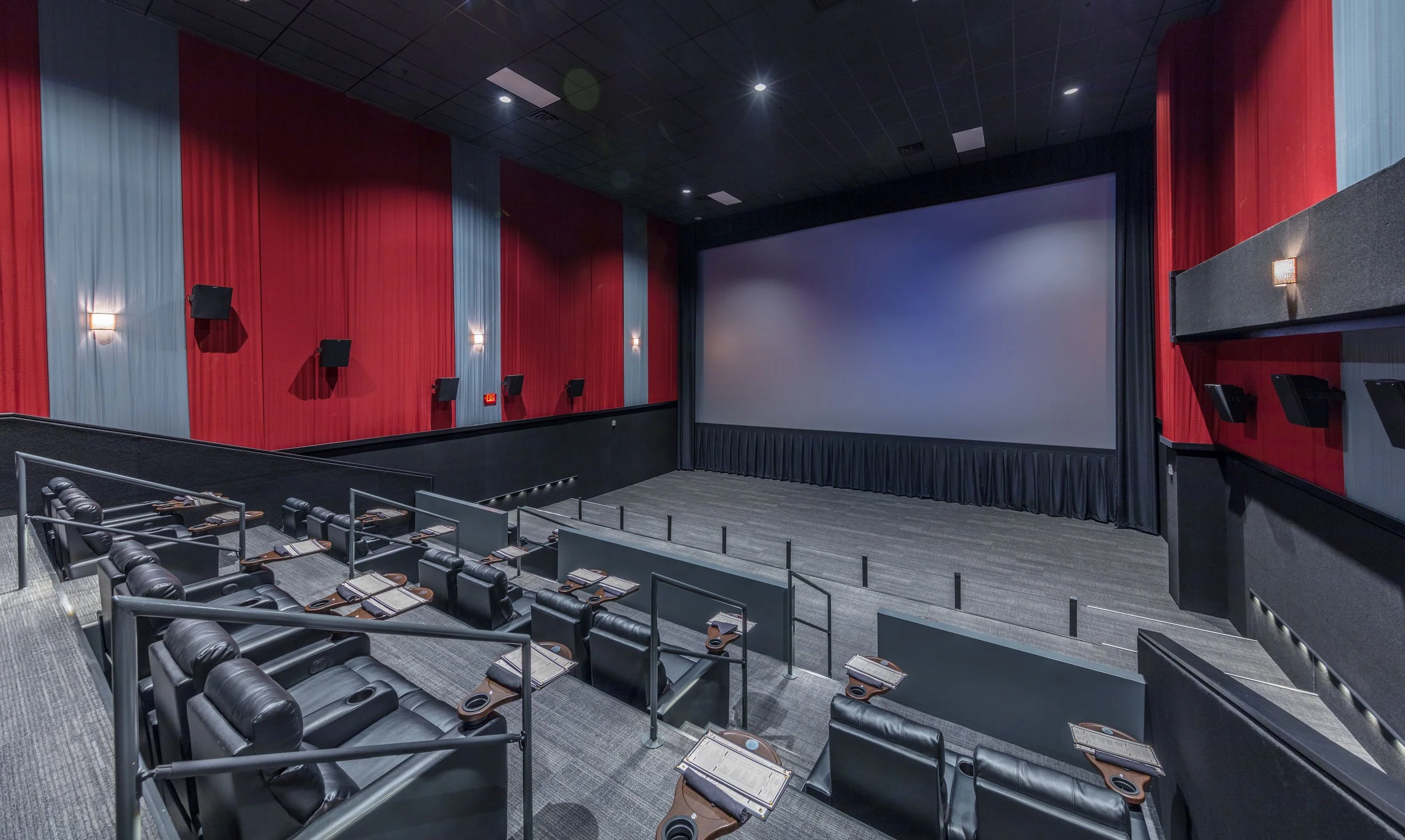 Interior of a modern movie theater showing room with black leather seats, a large screen, and red and gray curtain walls.