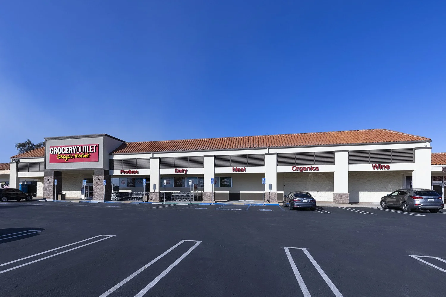 Exterior view of a grocery store called 'Grocery Outlet Bargain Market' with parking lot in front, no cars parked, and clear blue sky.