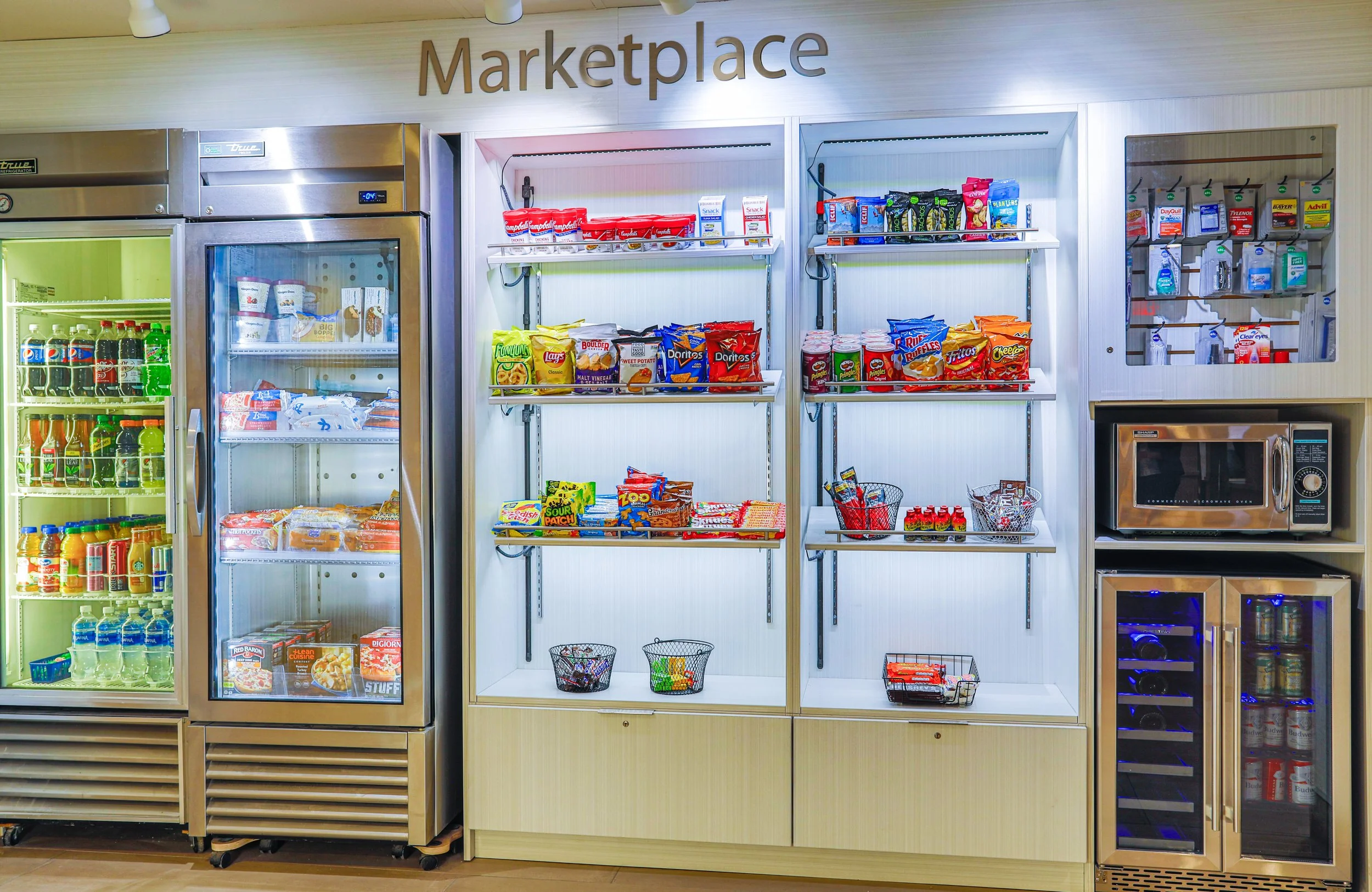 A vending area with snack shelves, a refrigerator with drinks, and a microwave oven.