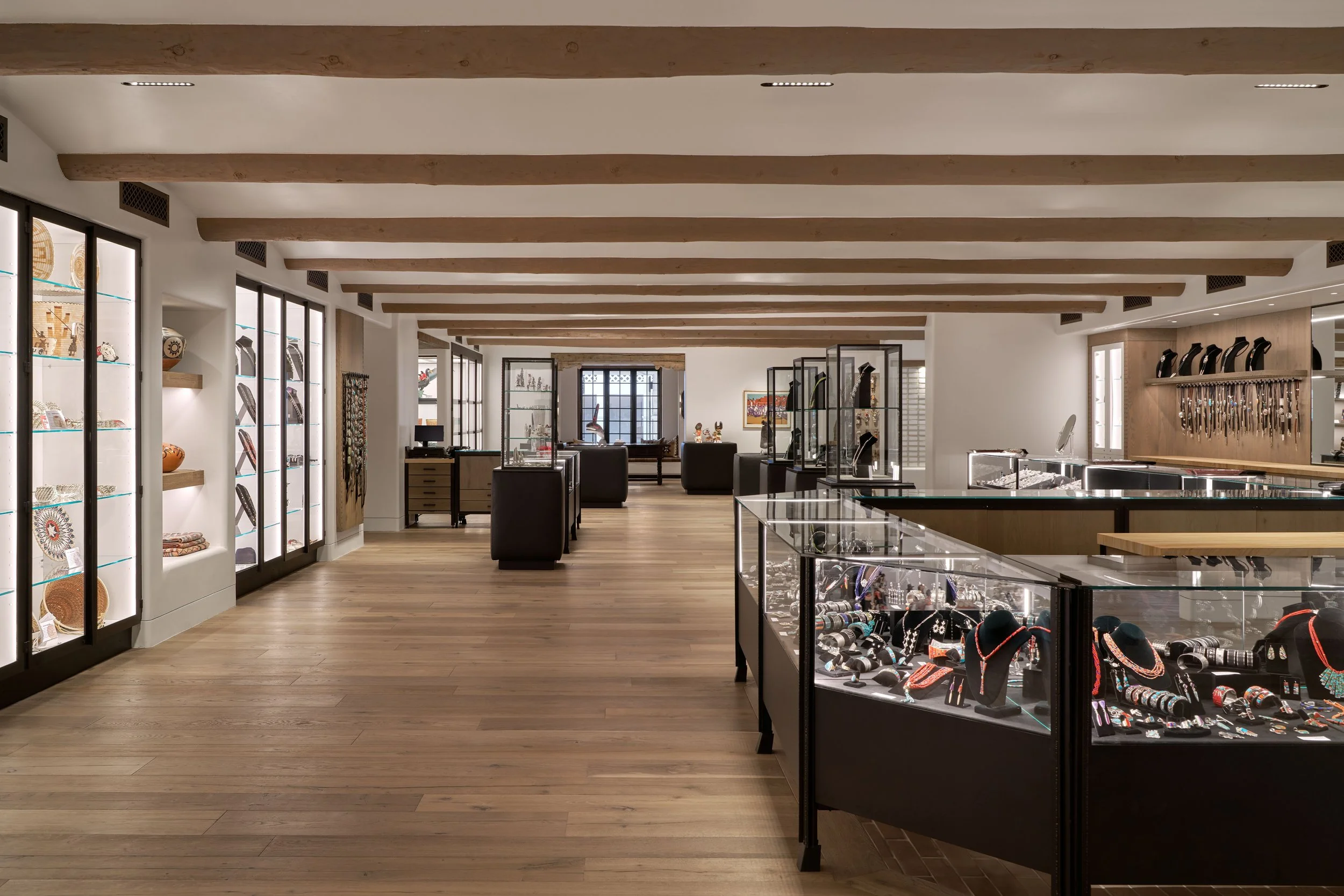Interior of a jewelry store with display cases holding necklaces, bracelets, and accessories, along with shelves and cabinets showcasing various items, in a well-lit space with wooden flooring and ceiling beams.