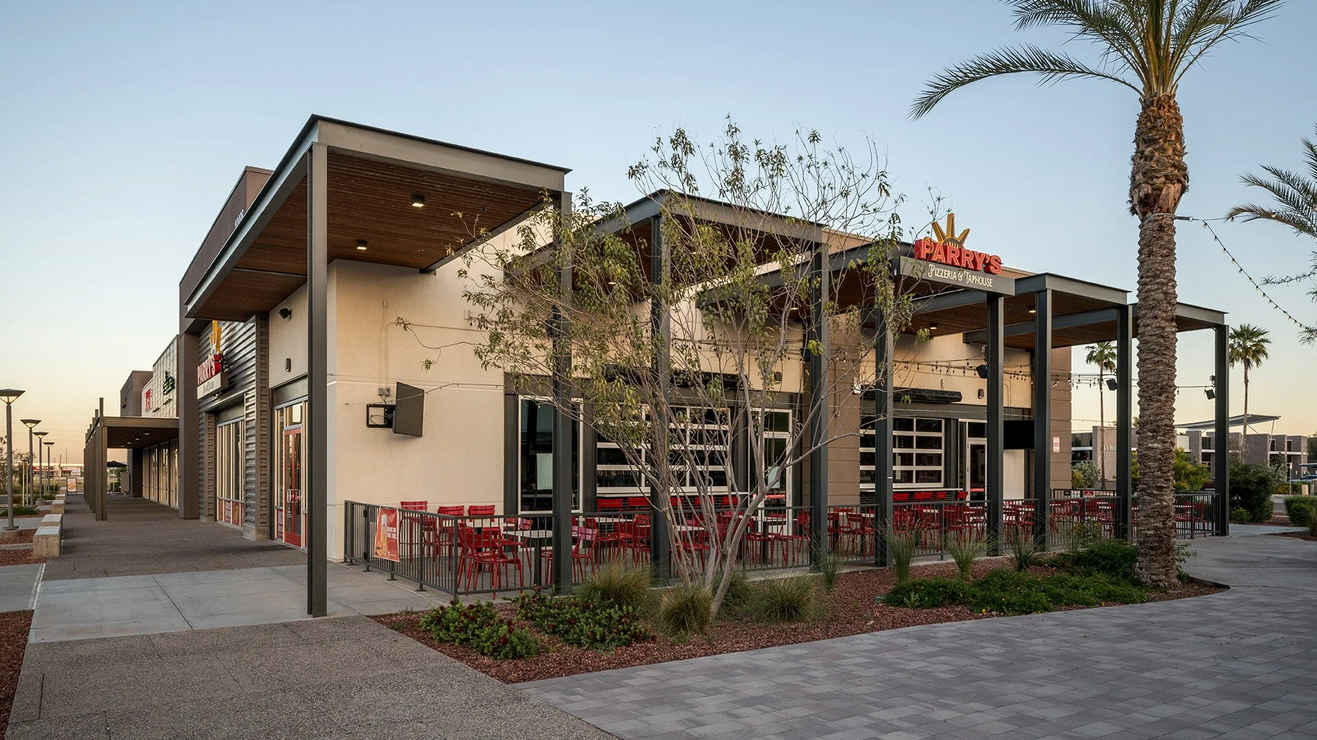 Exterior view of a modern commercial building with a patio area, palm trees, outdoor seating, and a sign for Parry's Pizzeria & Taproom.