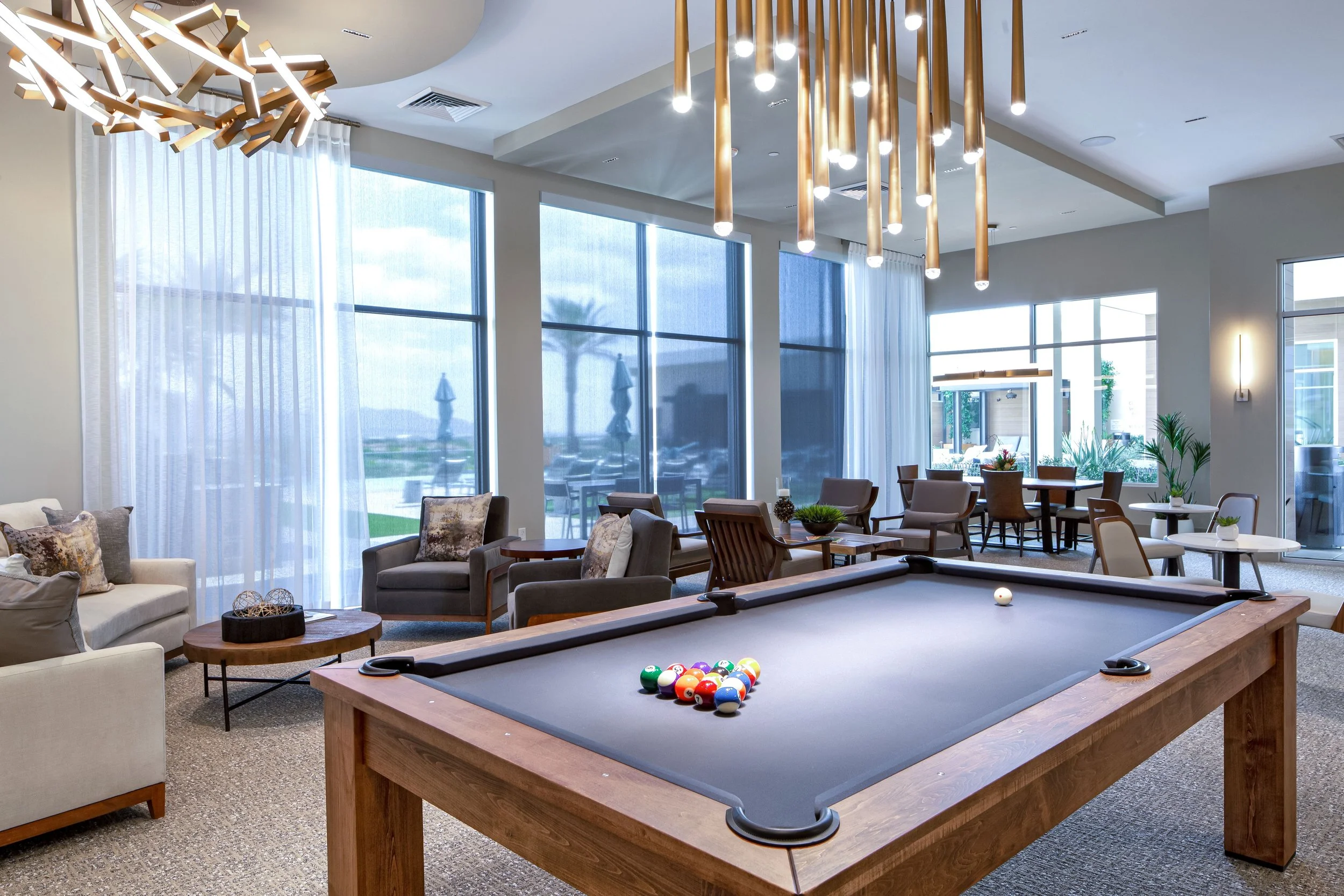 Indoor lounge area with a pool table, seating, and large windows letting in natural light