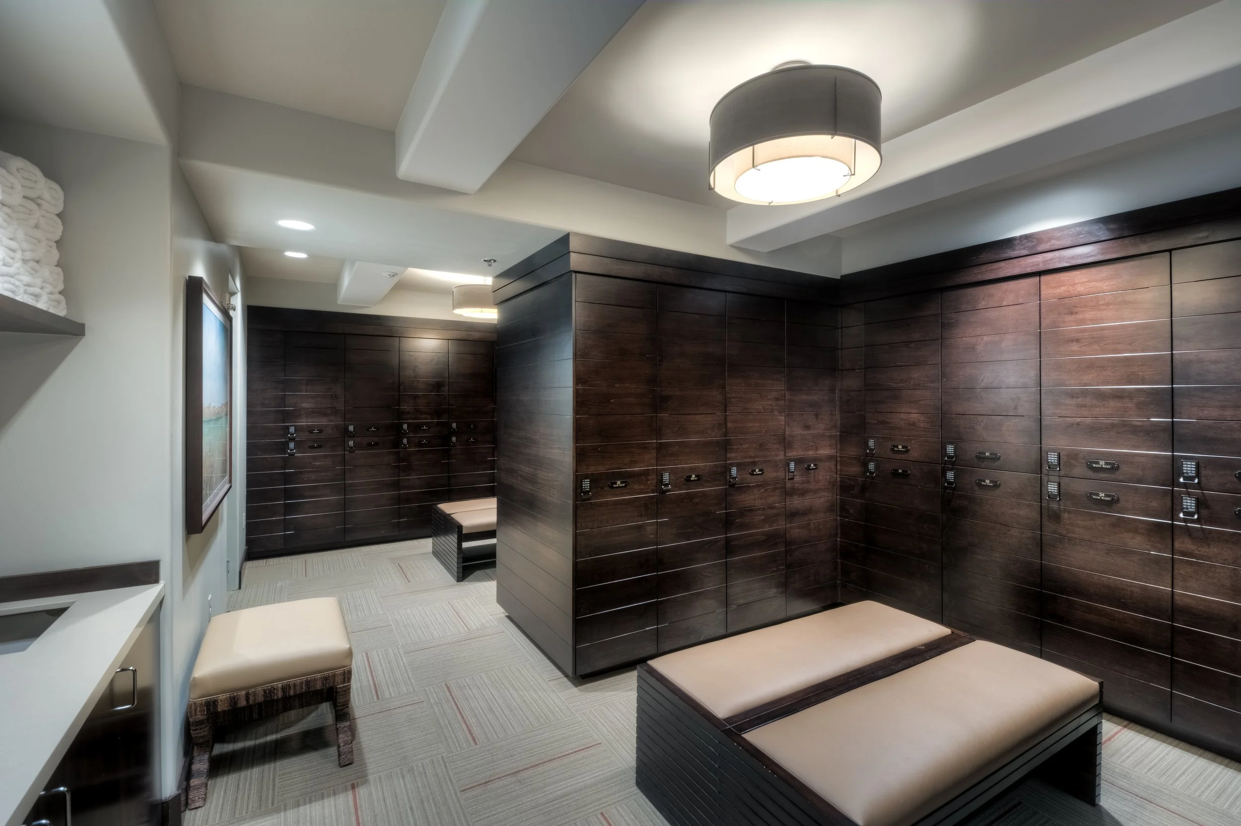 Locker room with dark wooden lockers, benches with cushions, and a beige carpeted floor.