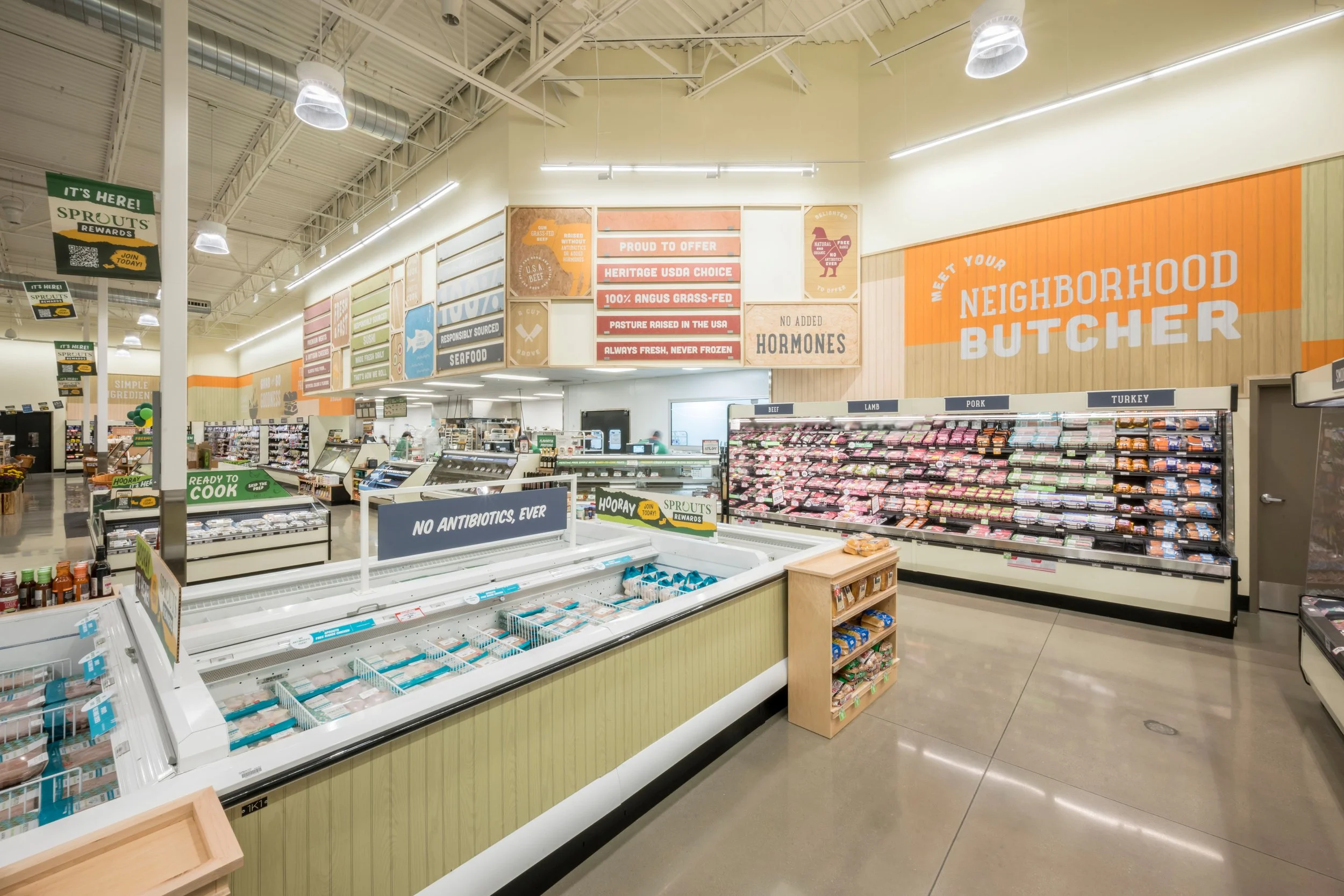 Interior of a grocery store with meat section, signs for beef, lamb, pork, and turkey, and colorful signs promoting locally sourced, hormone-free, and fresh meat.