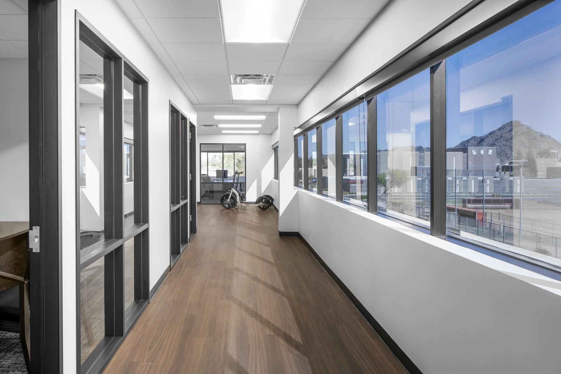 Empty office hallway with large windows, a stationary bike, and a mountain view outside.
