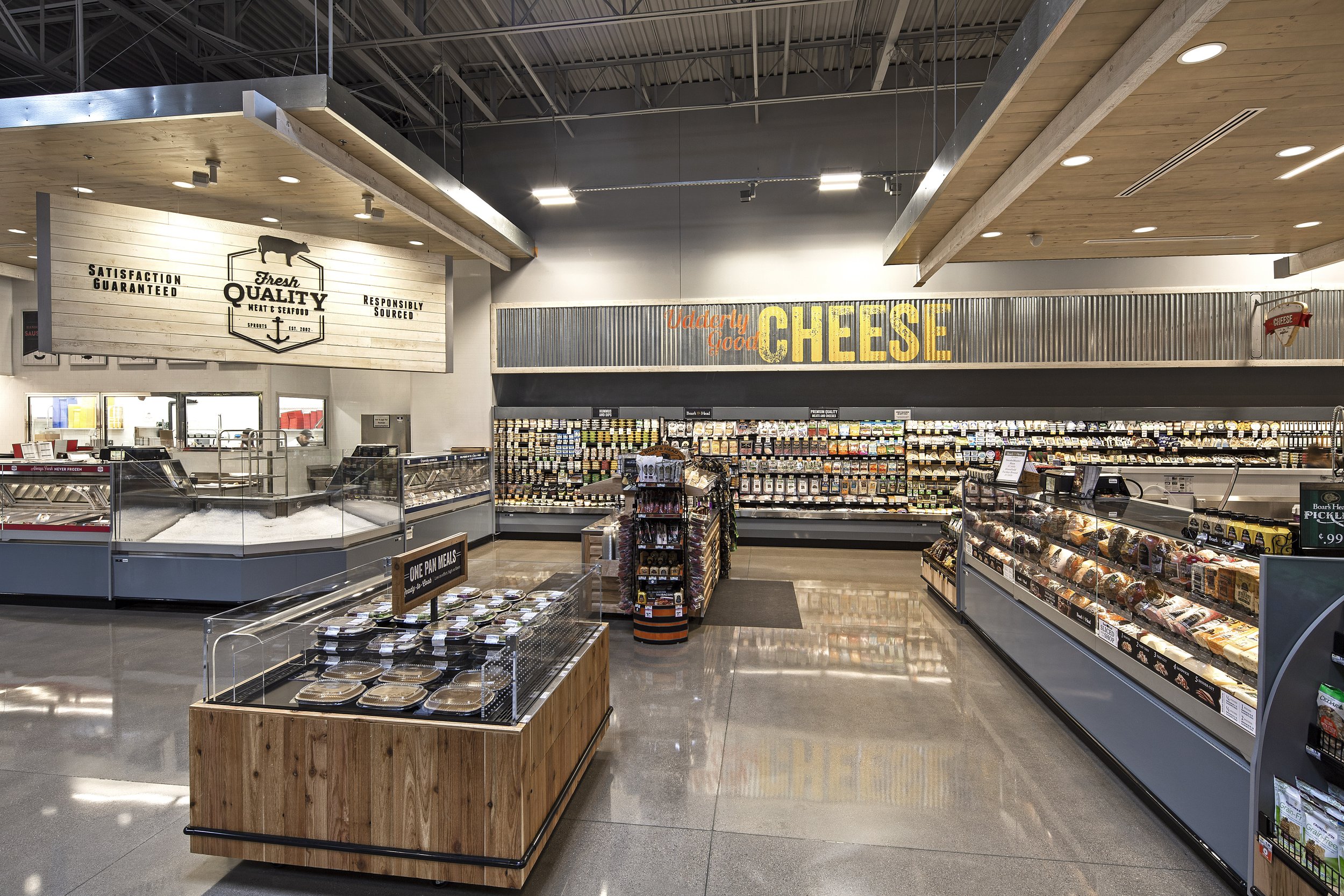 A grocery store interior with cheese section, refrigerated displays, a wooden display case with prepared meals, and signage reading "Valley Food Cheese" and "Fresh Quality."