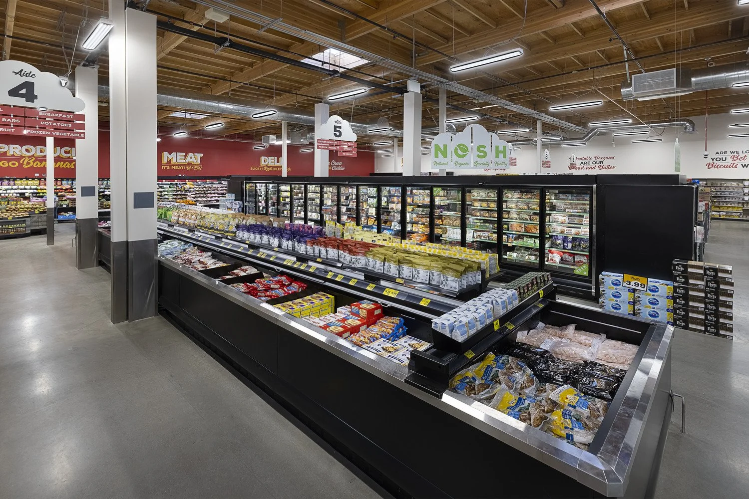 Interior of a grocery store featuring refrigerated frozen food section with various packaged items, supermarket signage, and aisles in the background.