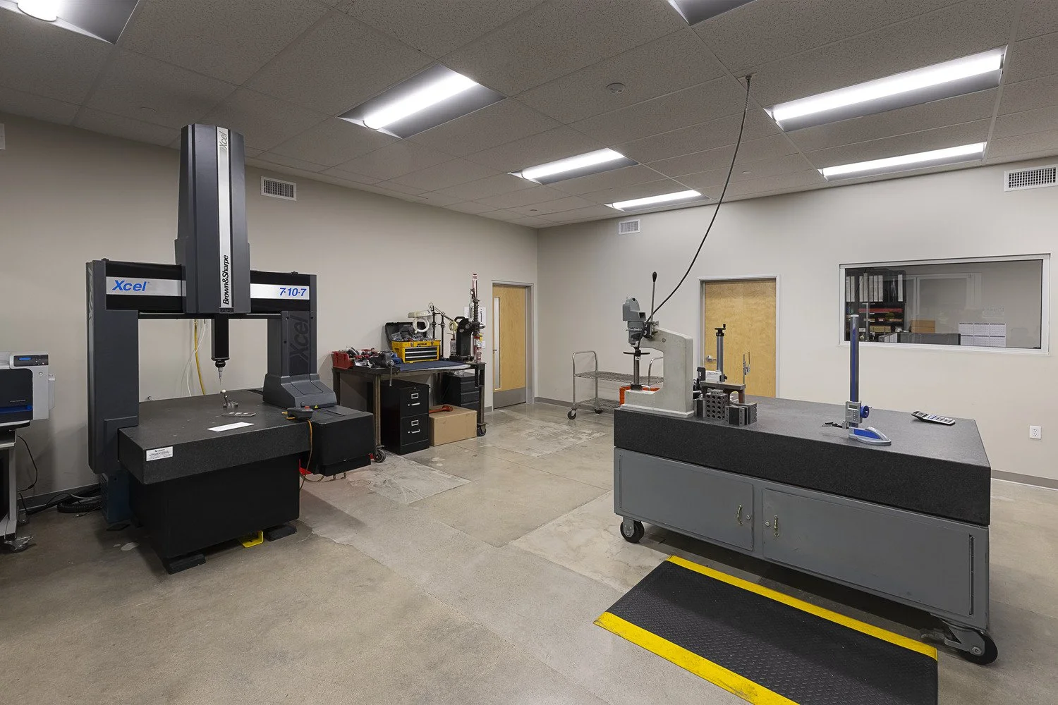 Laboratory or manufacturing room with precision measurement equipment, tools, and workbenches, featuring a large robotic arm and various calibration devices.
