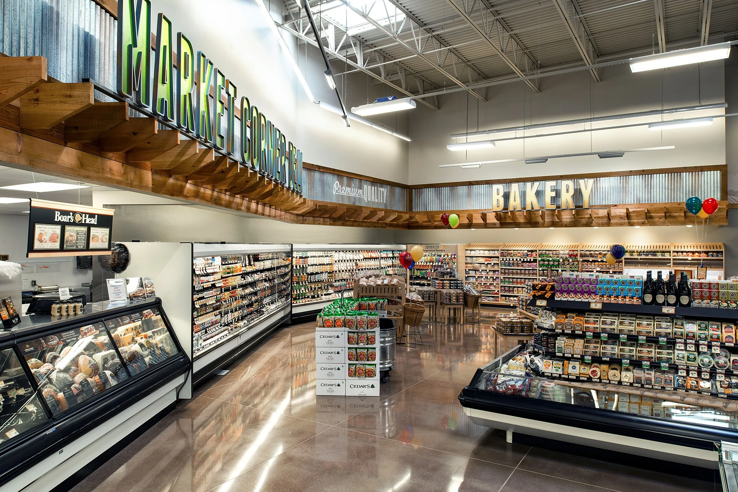 Interior of a grocery store's bakery section with shelves stocked with baked goods, balloons, and a wooden sign overhead reading 'Bakery'.