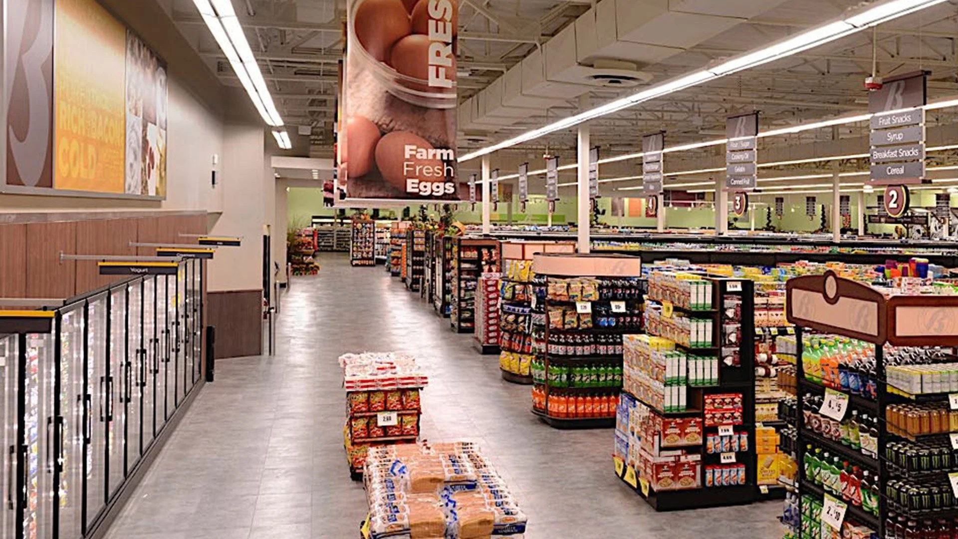 A grocery store aisle with signs for fresh eggs at the front and other sections labeled for fruit snacks, syrup, breakfast snacks, cereal, and more, shelves stocked with various food products, and a large hanging banner showing farm fresh eggs.