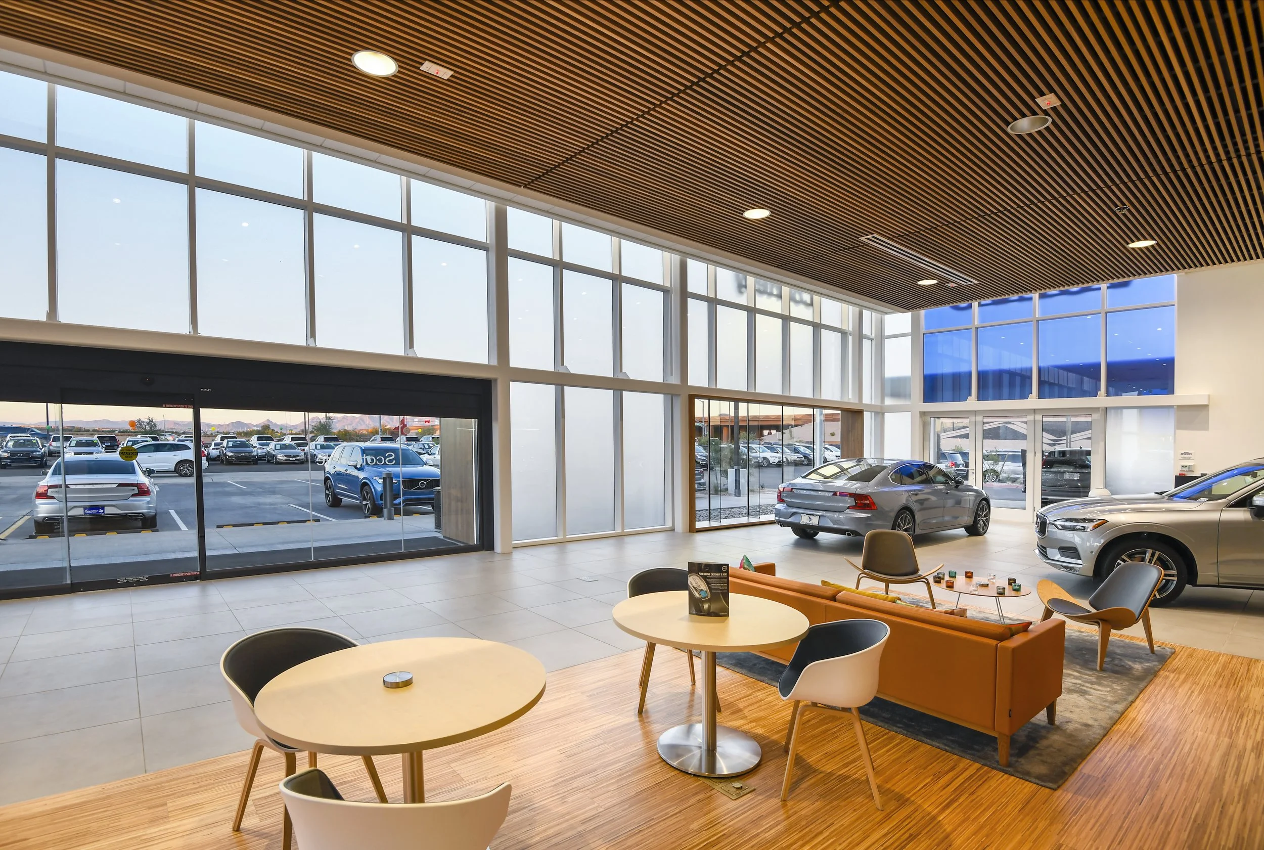 Car dealership showroom with large glass windows, cars on display, reception area with seating.
