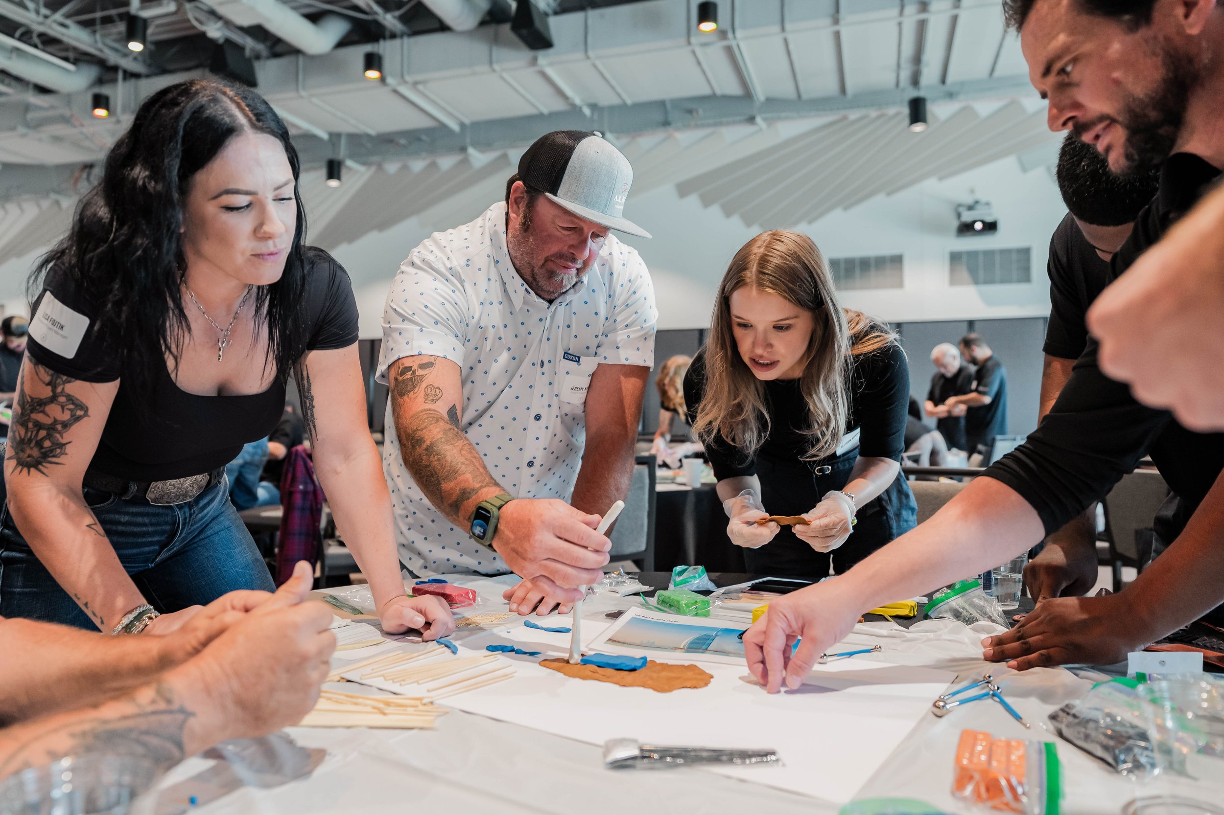 Group of people gathered around a table working on a project, some holding tools, in a modern indoor space.