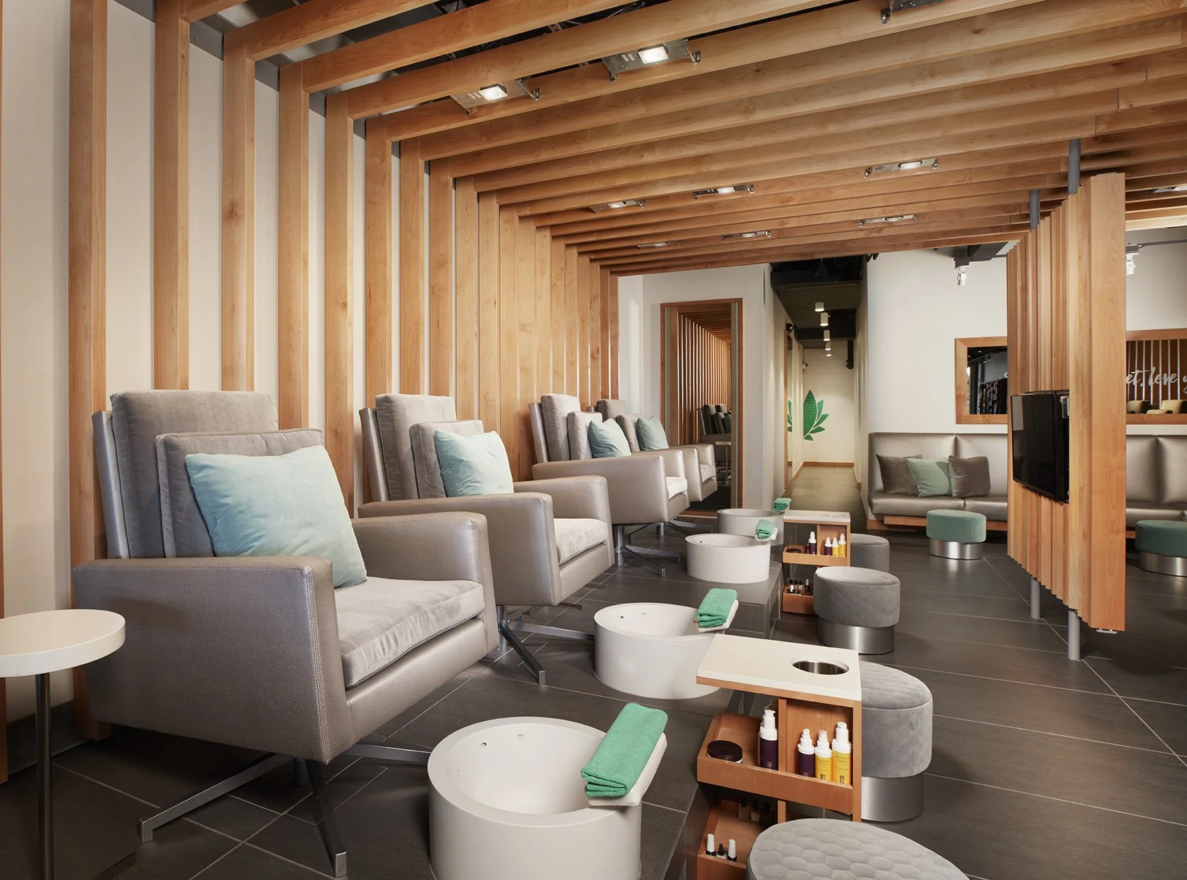 A modern spa or salon with massage chairs, foot baths, and skincare products, featuring wooden ceiling beams and a cozy interior design.