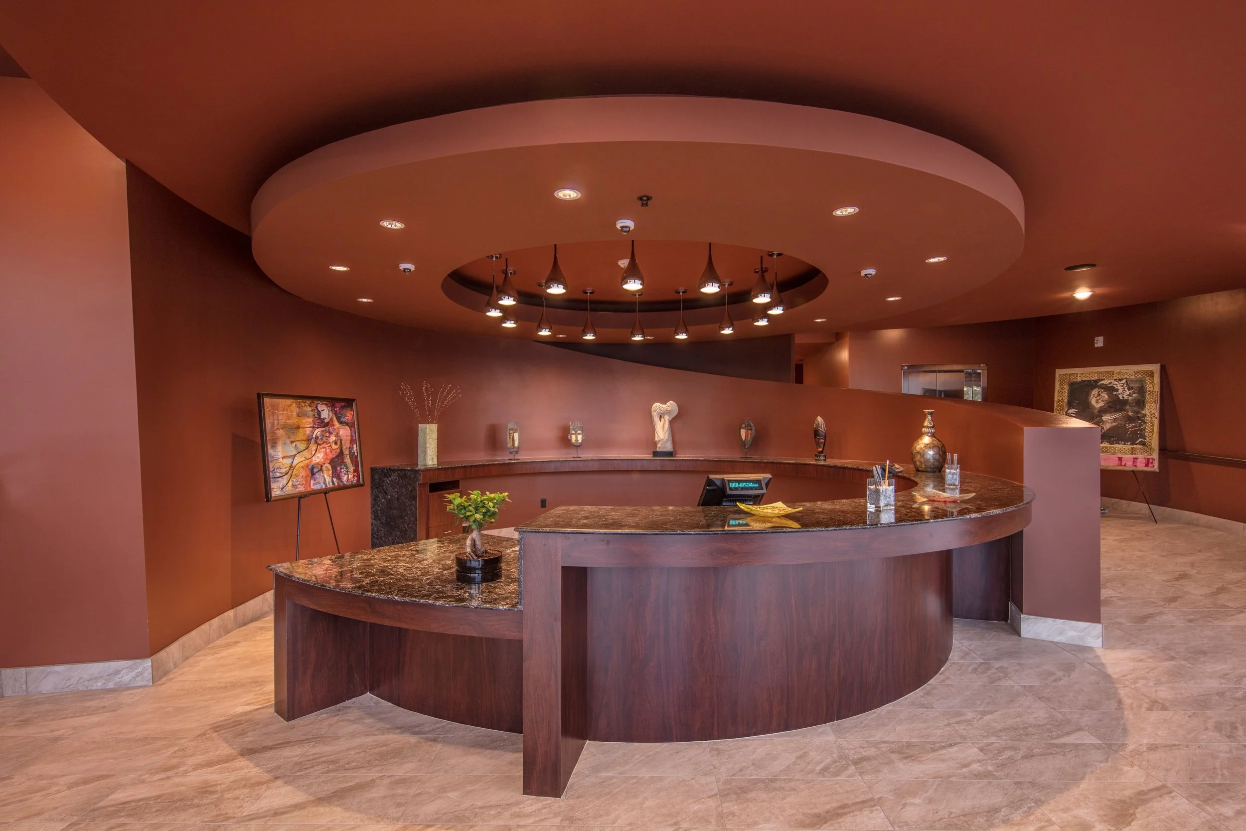 Luxurious hotel lobby reception area with a curved dark wood front desk, decorative vases, artwork, and flowers on the wall.