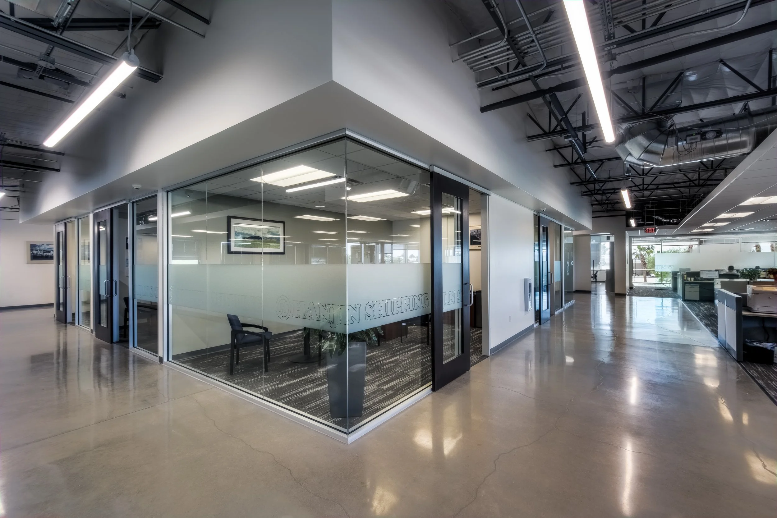 Empty office hallway with glass-walled conference rooms and overhead lighting.