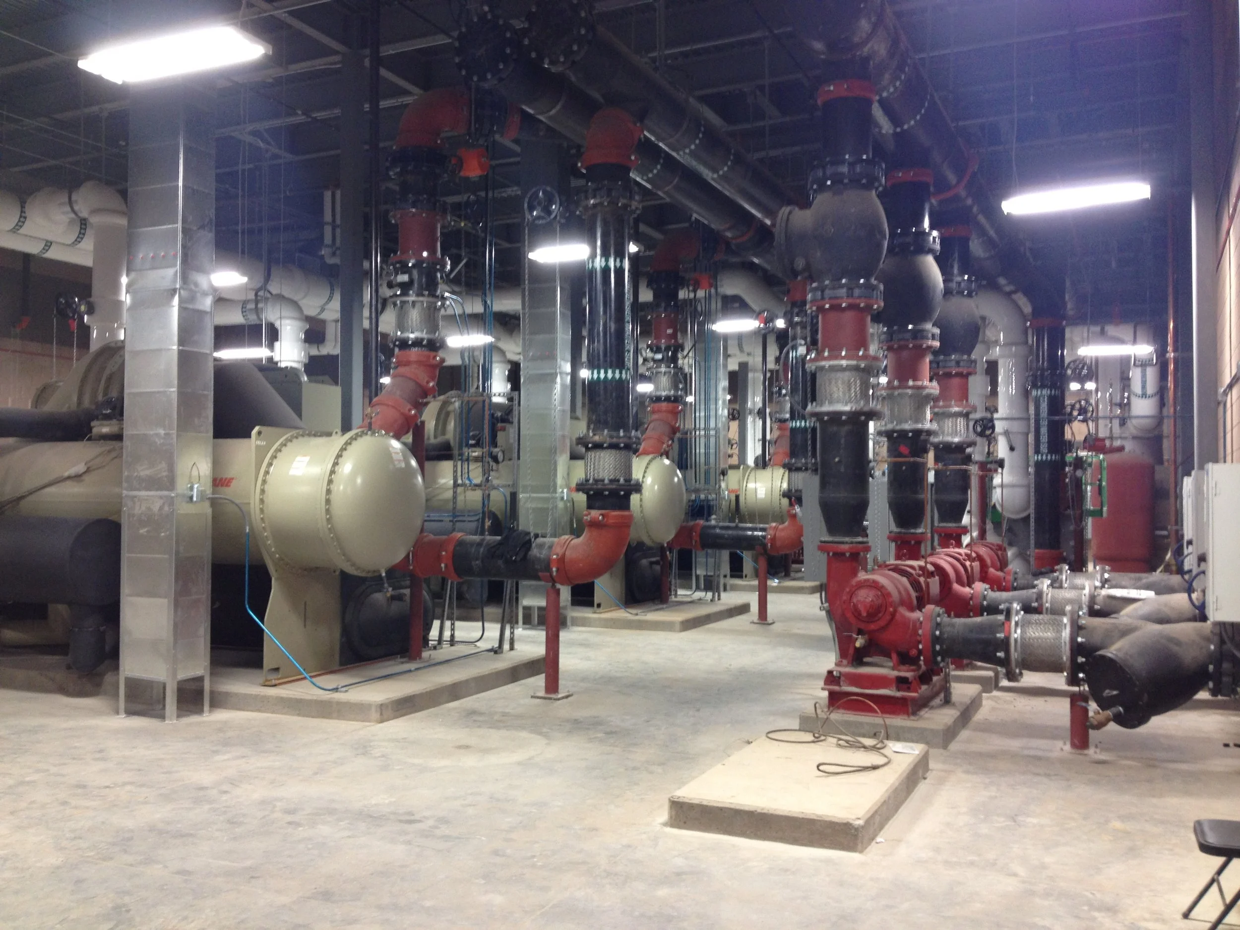 View of a mechanical room with various pipes, valves, and large equipment for industrial use.