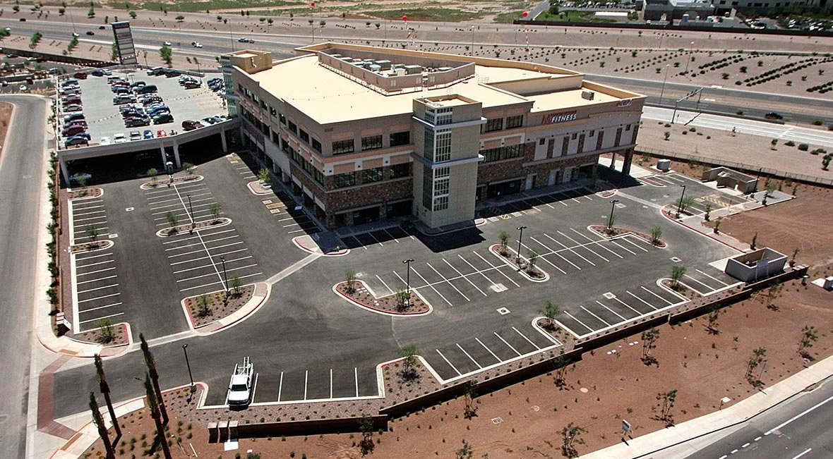 An aerial view of a large, multi-story commercial building with a parking lot, surrounded by desert landscaping and roads.