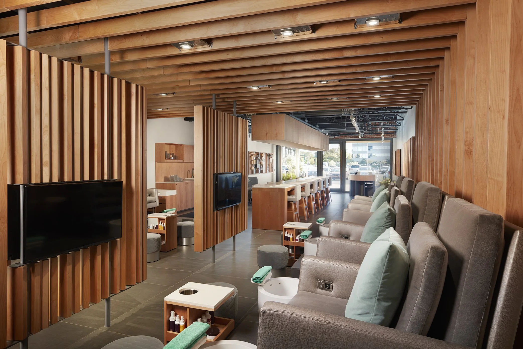 Modern nail salon with pedicure stations, massage chairs, and a reception area, featuring wooden accents and large front windows.