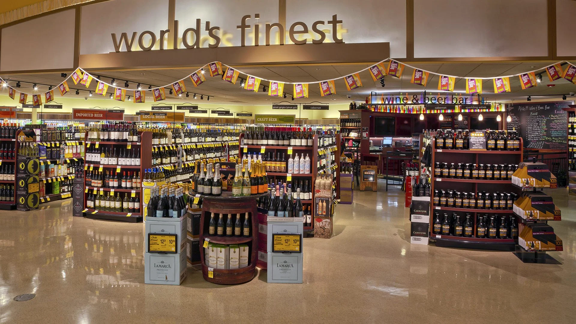 Interior of a grocery store with sections for imported, local, and craft beer, and a wine and beer bar in the background.