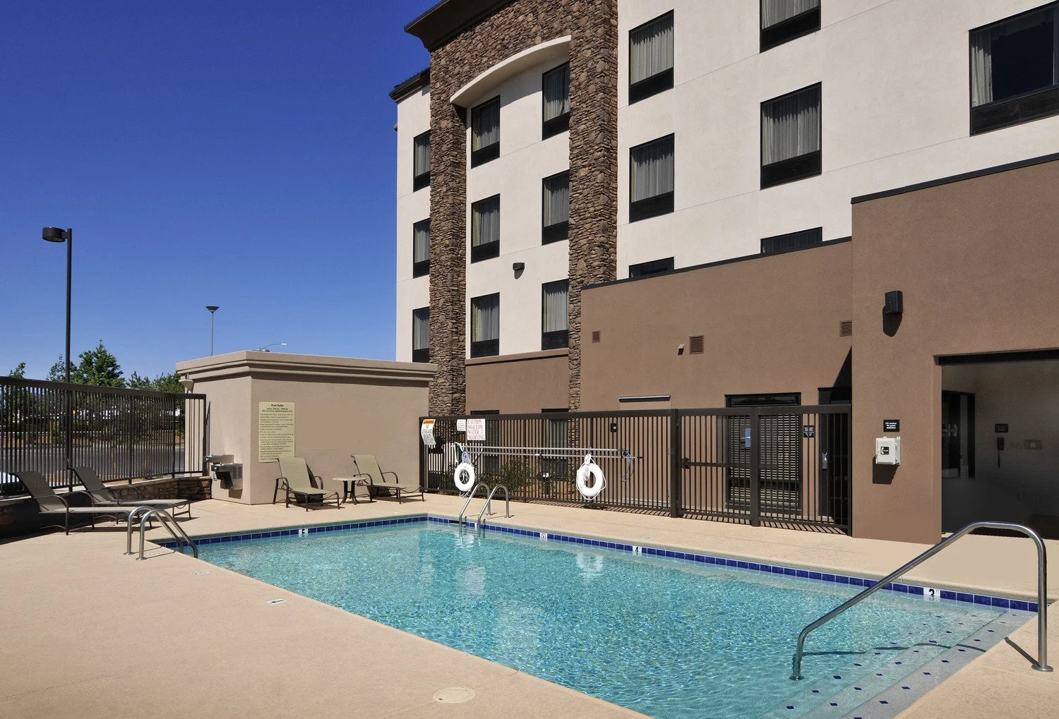 Outdoor swimming pool area with lounge chairs and building in the background.