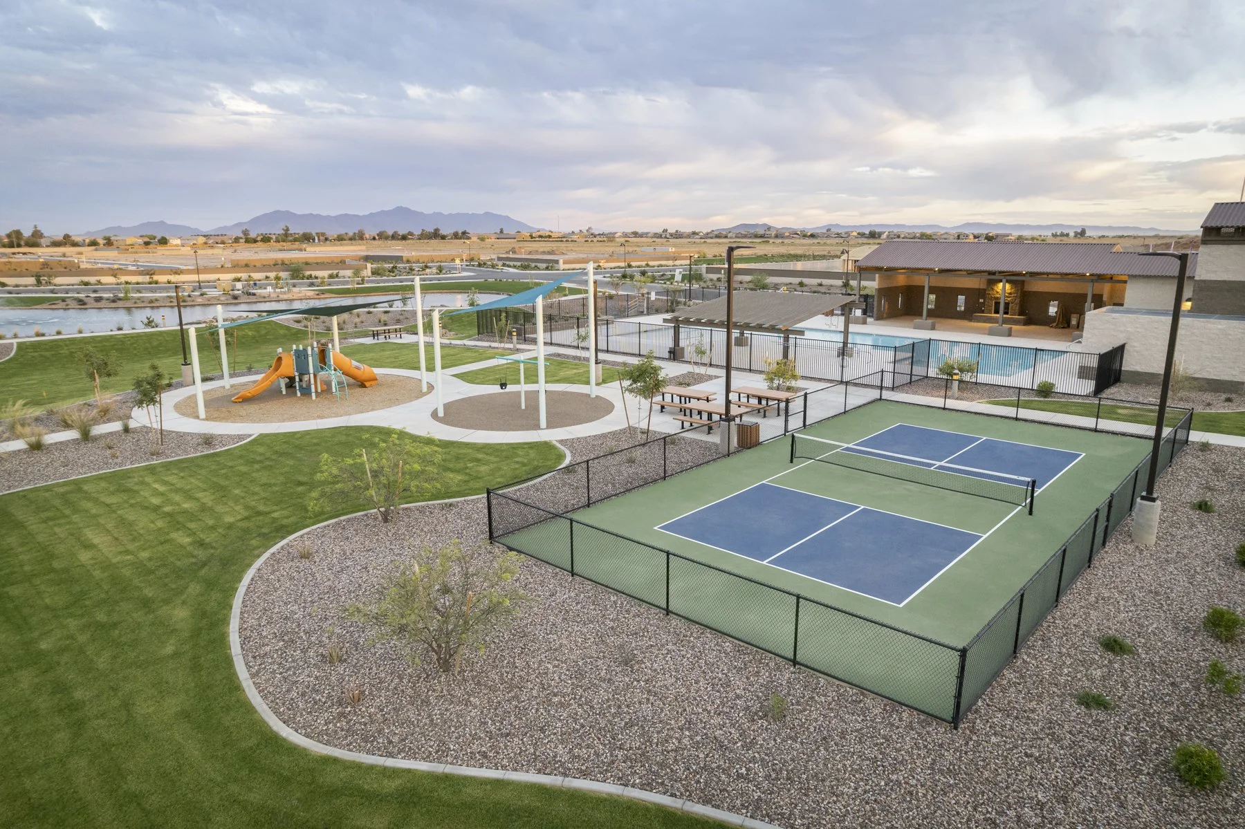 Community outdoor recreation area with a children's playground, tennis court, picnic tables, a swimming pool, and scenic mountain views in the background.