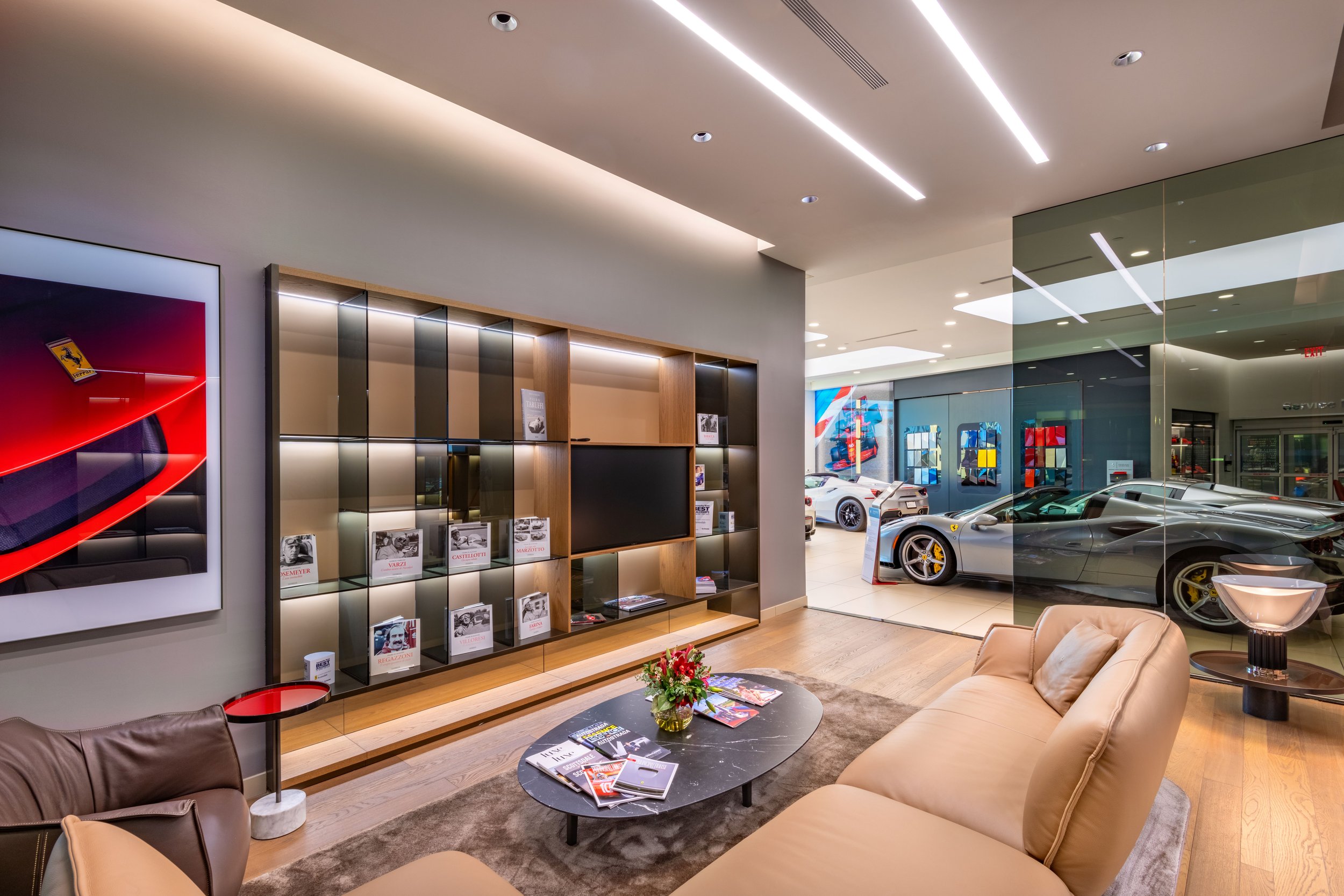 Luxury car showroom with a modern seating area, glass partition, and several high-end cars on display.