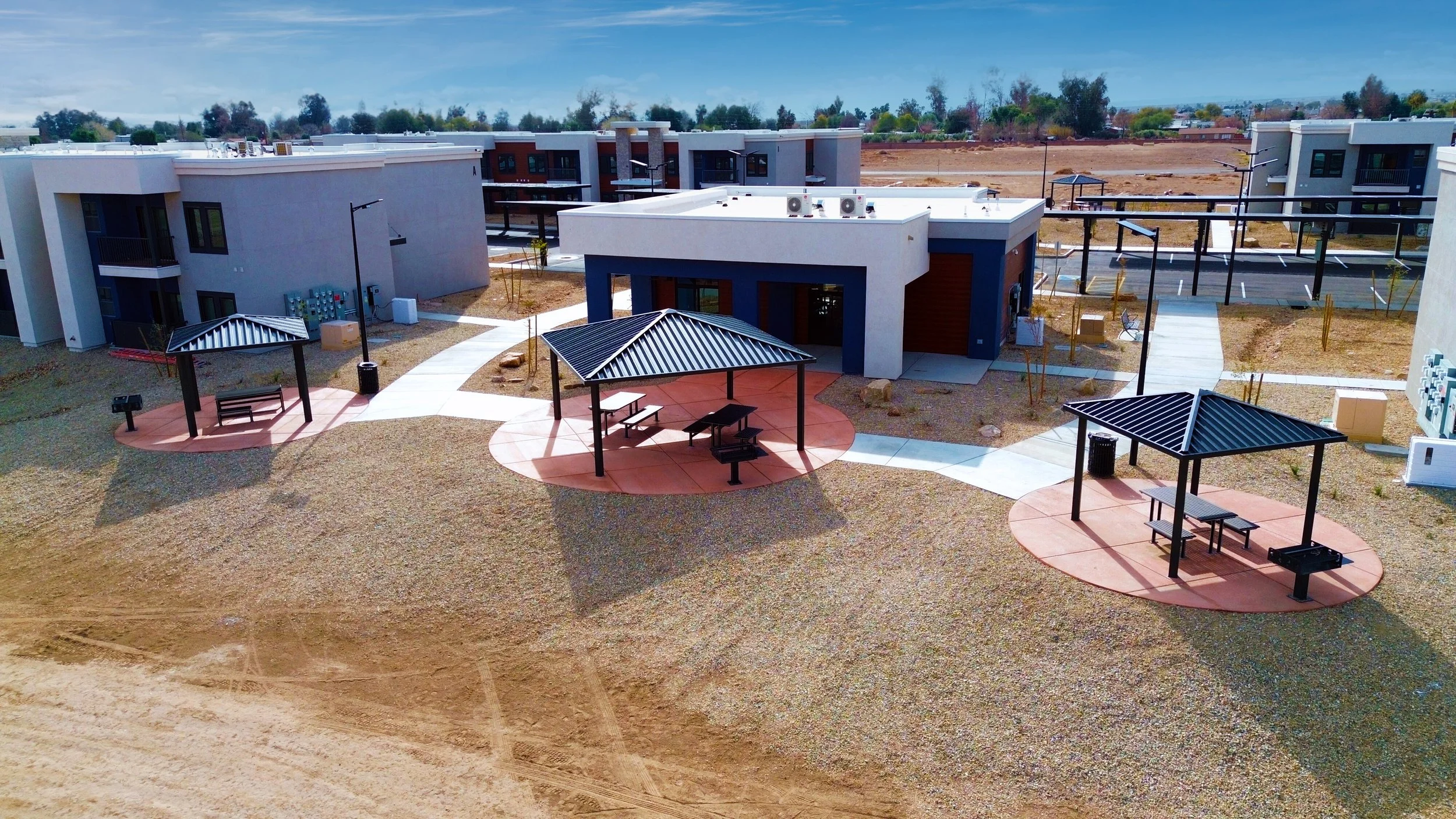 Aerial view of modern apartment complex with multiple buildings, paths, and shaded picnic areas with grills and seating.
