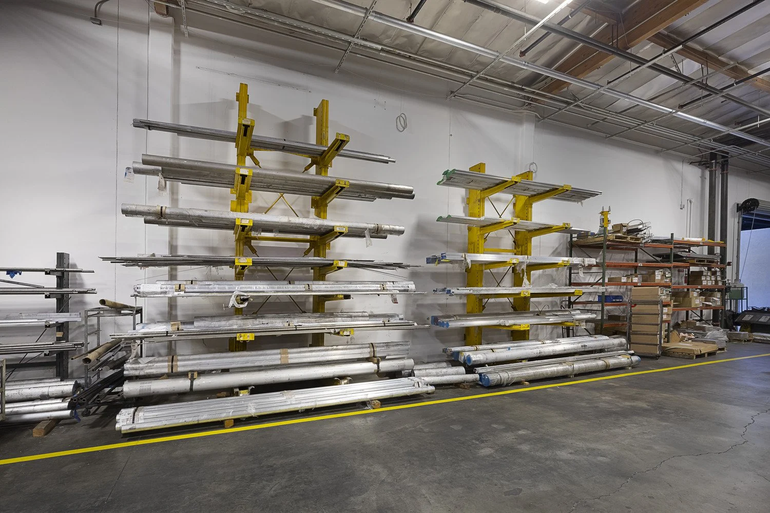 Metal pipes and construction materials organized on yellow and gray shelving units in a warehouse.
