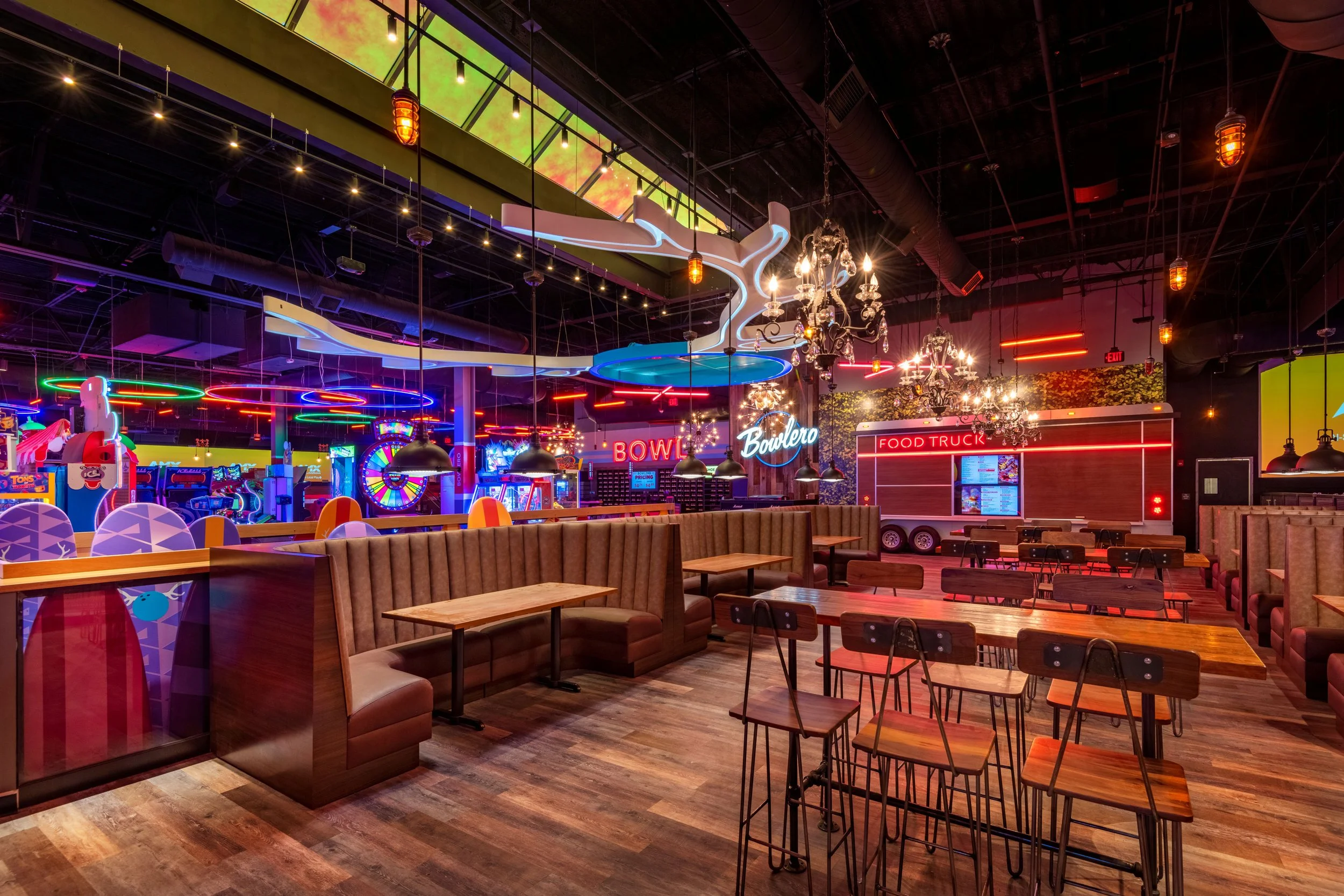 Interior of a colorful arcade with neon signs, arcade games, and seating areas including booths and tables.