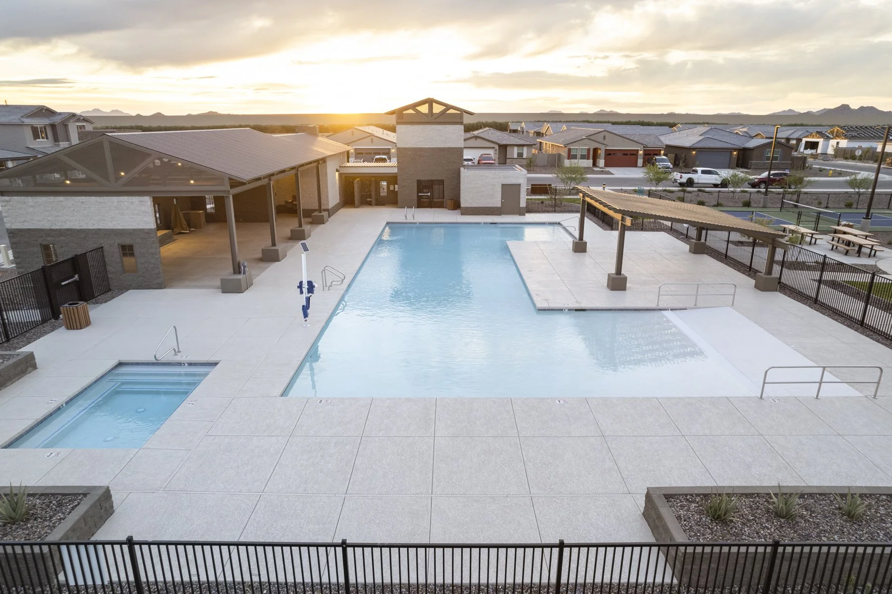 Empty swimming pool and a hot tub at sunset in a residential community pool area, with a shaded pavilion and nearby pathways.
