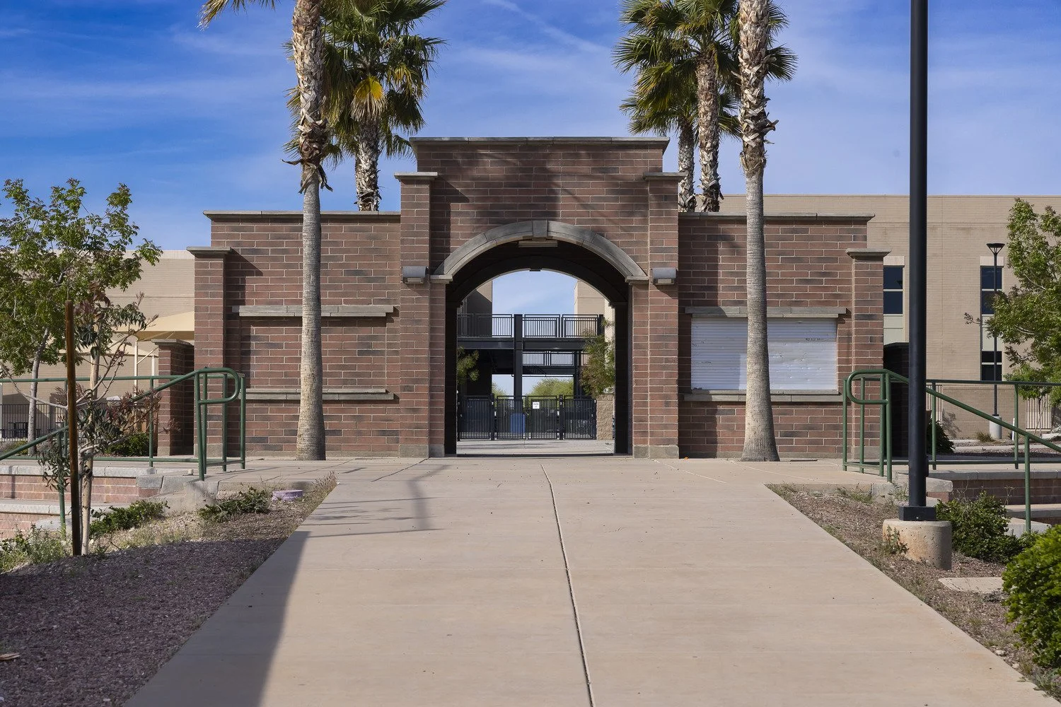 A brick building with an arched entranceway, surrounded by palm trees and a concrete pathway in front.
