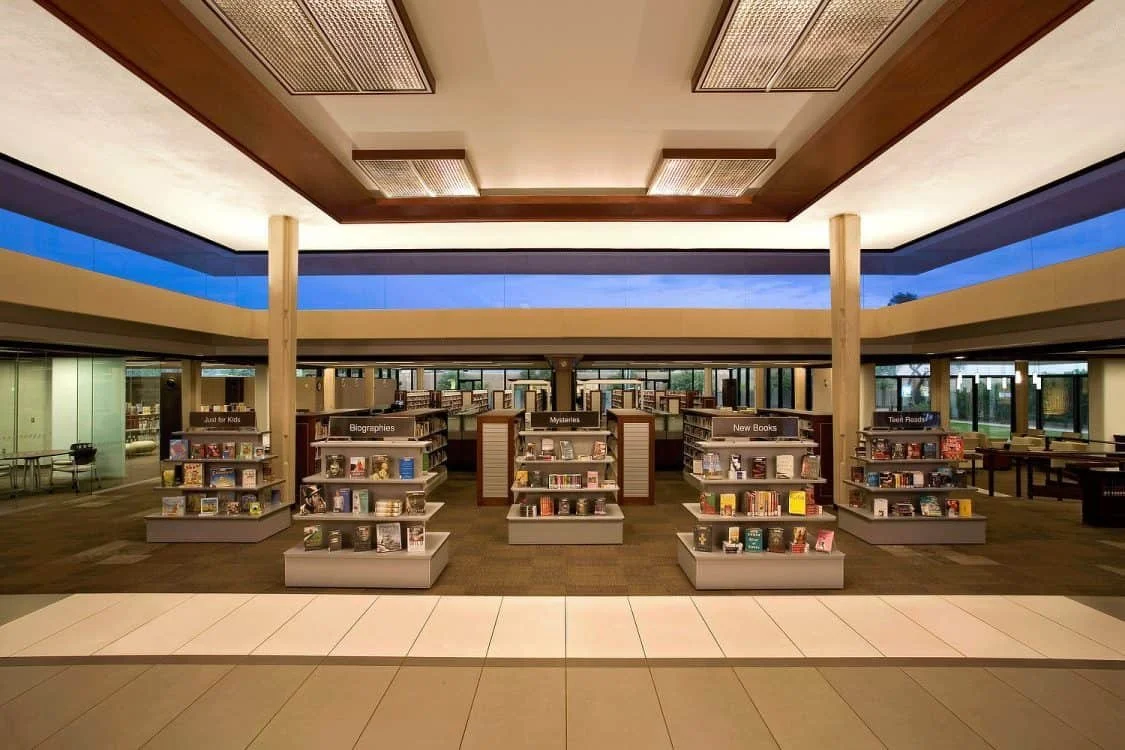 Interior of a modern library with bookshelves, categorized sections, and a reading area.
