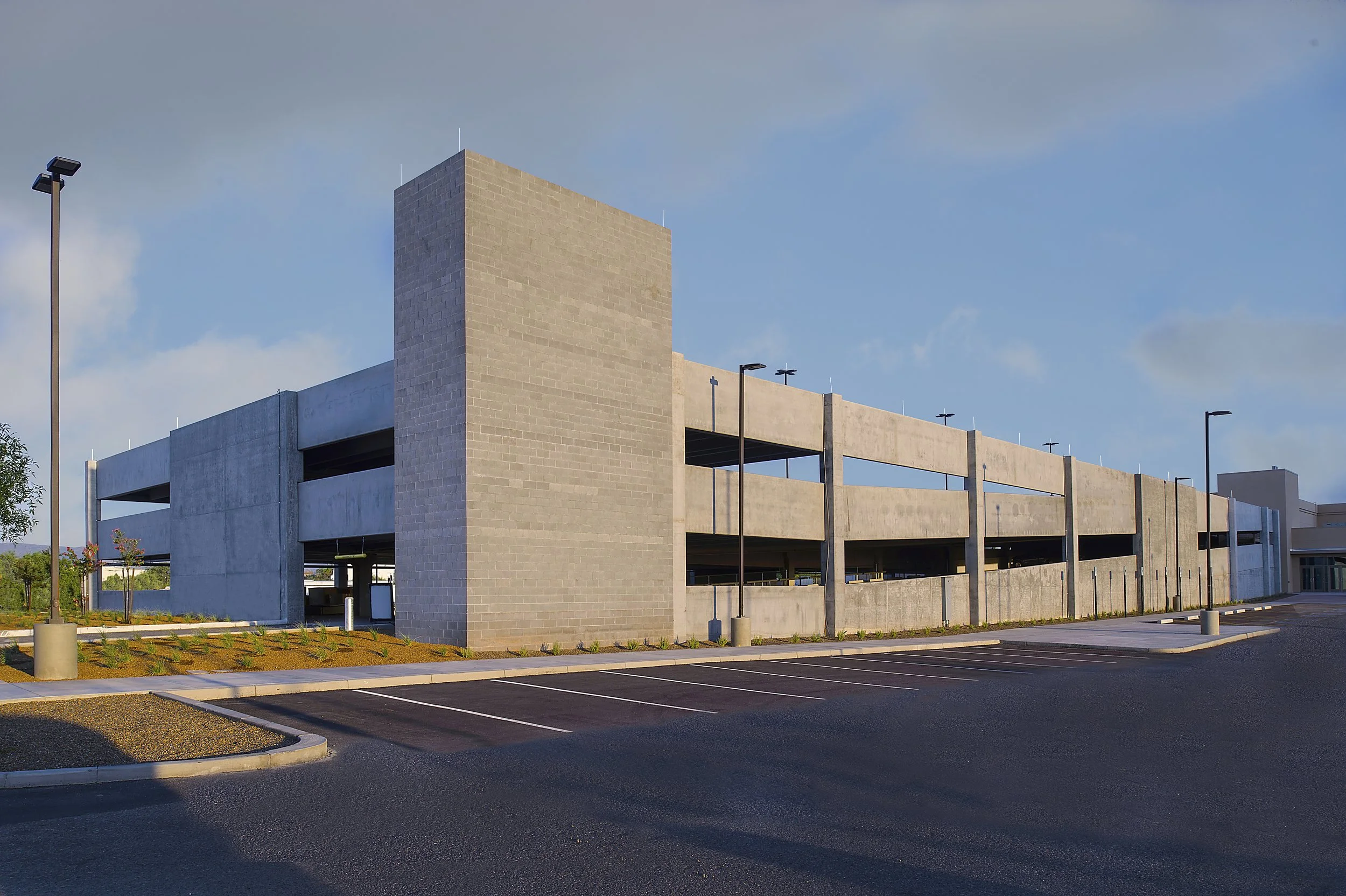 Empty parking lot in front of a modern concrete building structure with parking garage levels, surrounded by streetlights and a clear sky.