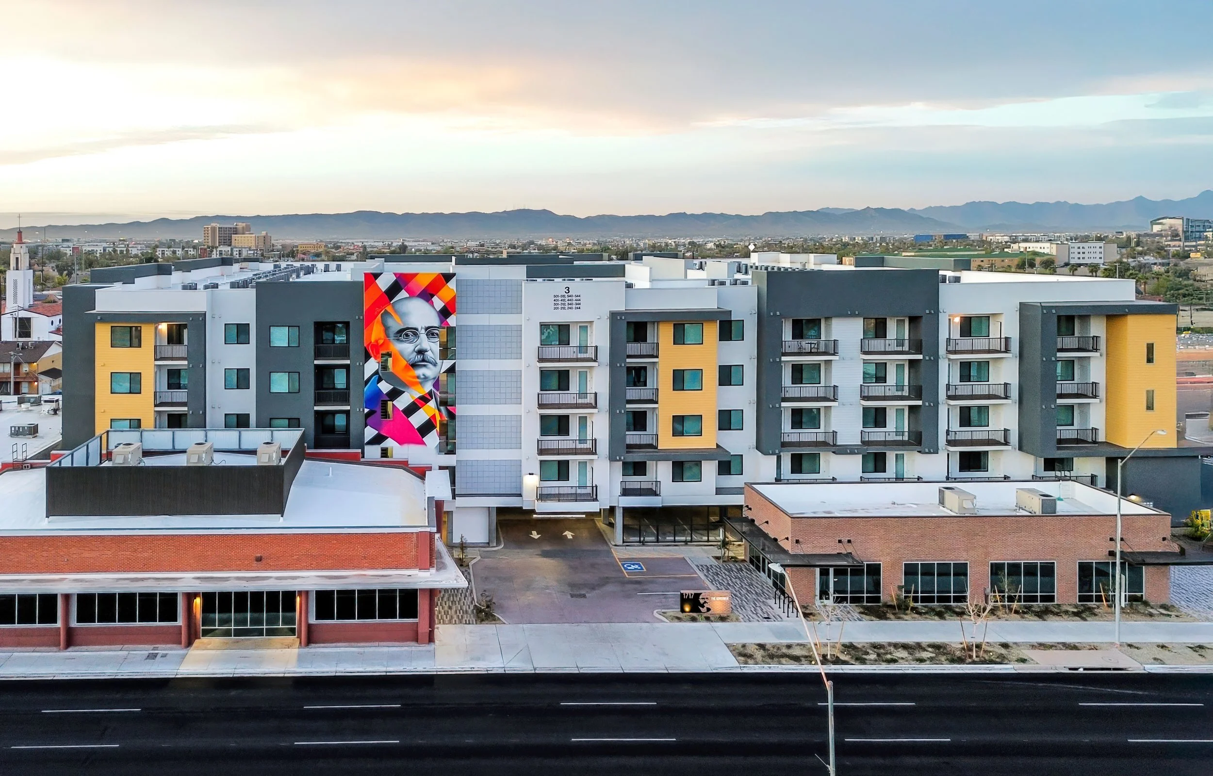 Colorful mural of a man with glasses on a modern apartment building with mountains and city in the background
