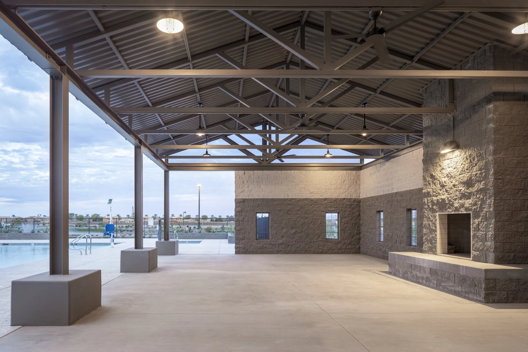 Empty outdoor covered pavilion near swimming pool with brick wall, small windows, and ceiling fans