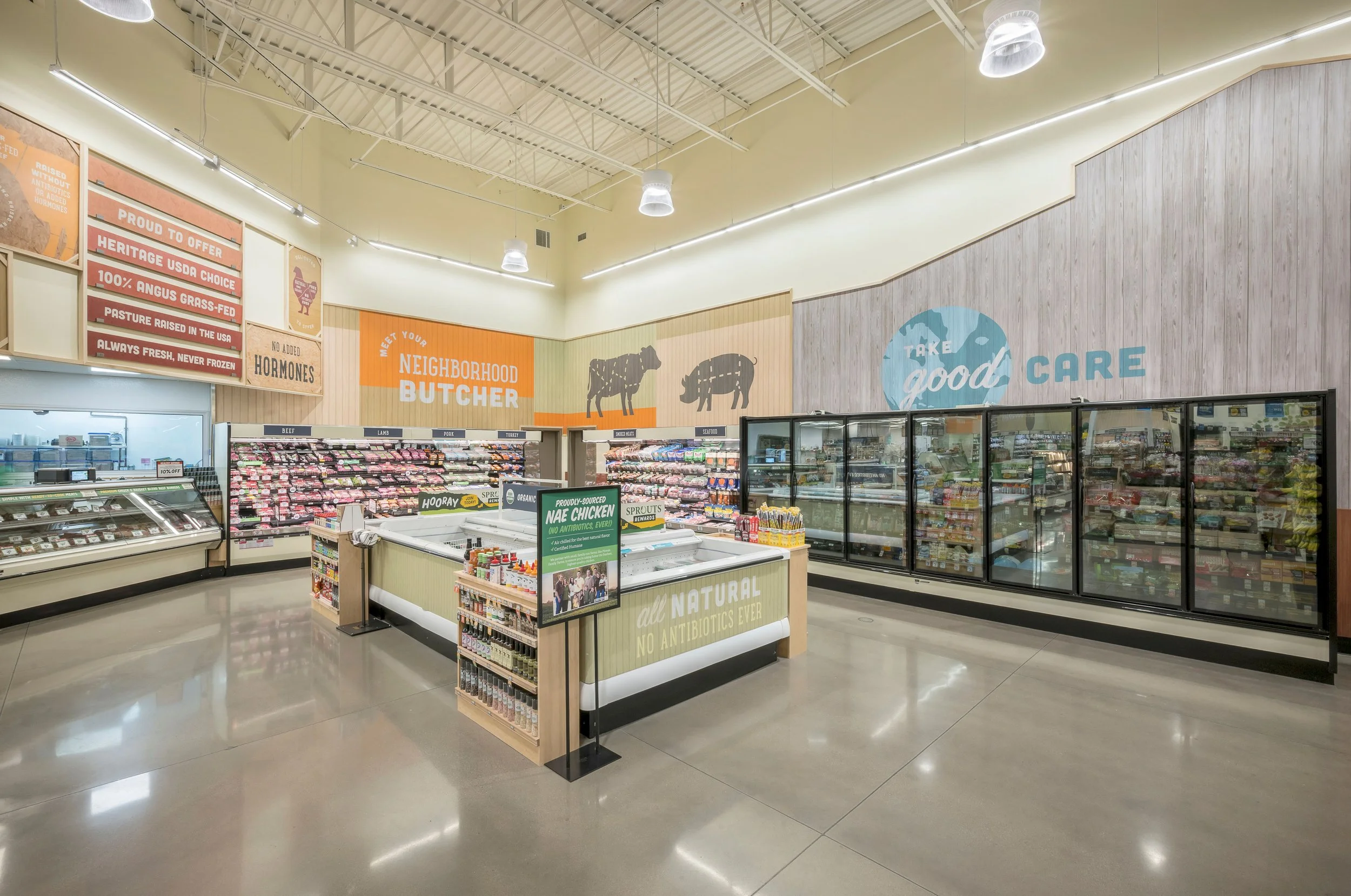 Interior of a modern grocery store with fresh meat displays, frozen foods in glass freezers, and signage promoting local and natural products.