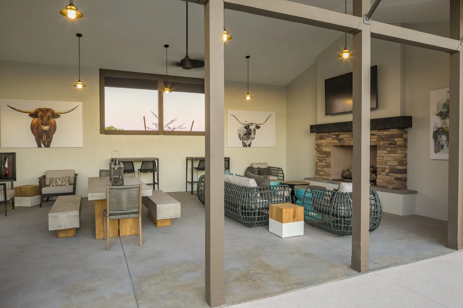 Indoor lounge area with contemporary furniture, art depicting highland cattle, a brick fireplace, wall-mounted TV, and large windows.