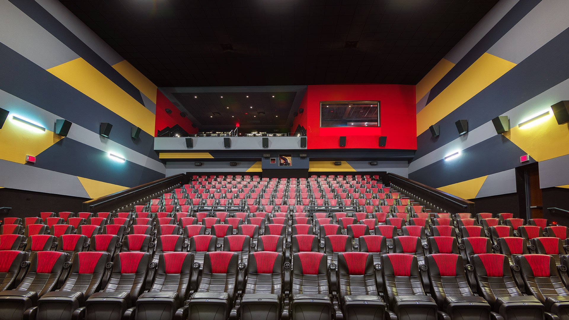Empty movie theater with red and black seats, colorful striped walls, and a screen in the background.