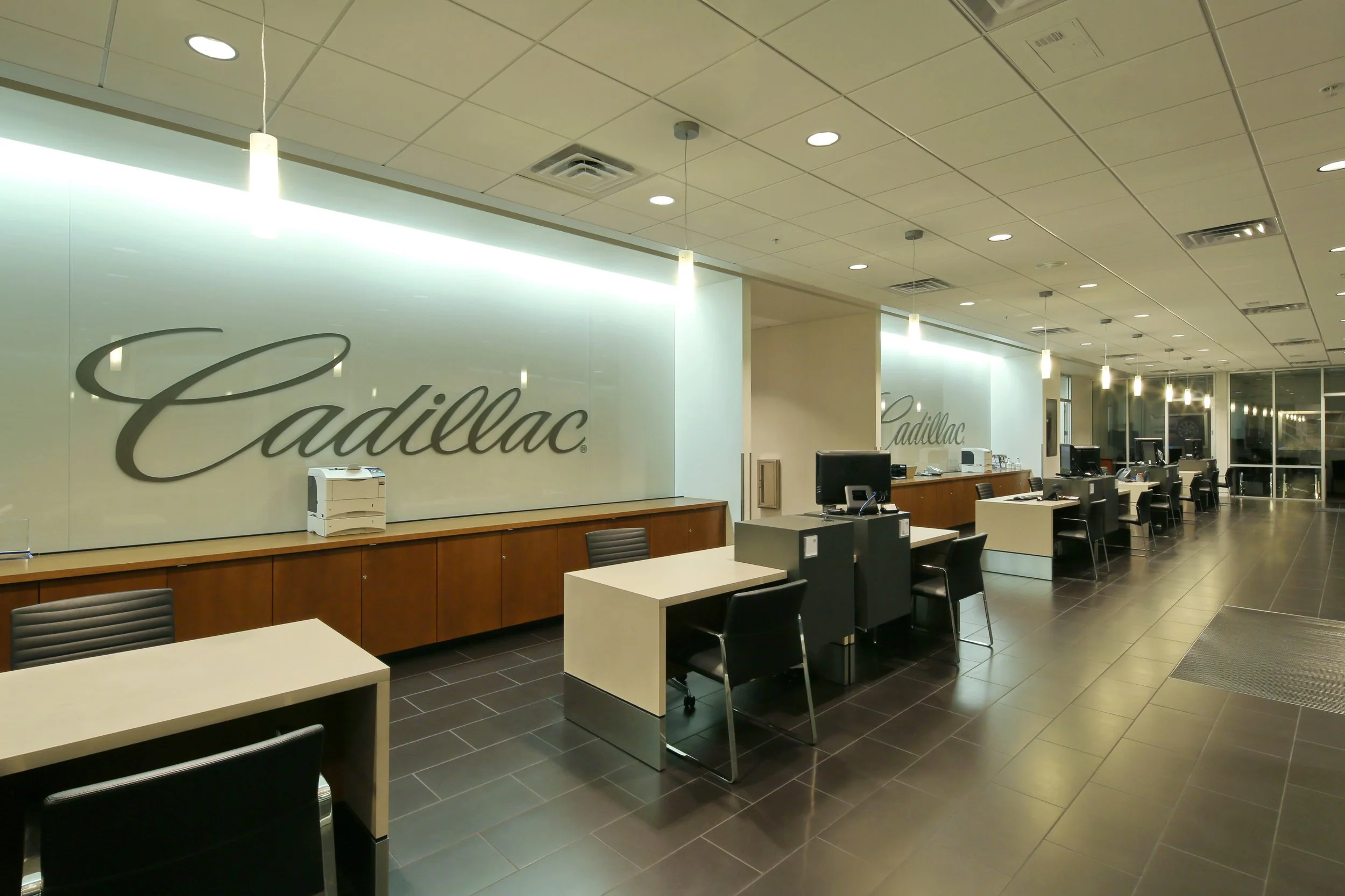 Cadillac Arrowhead dealership show room with desks, computers, and the Cadillac logo on a glass wall.