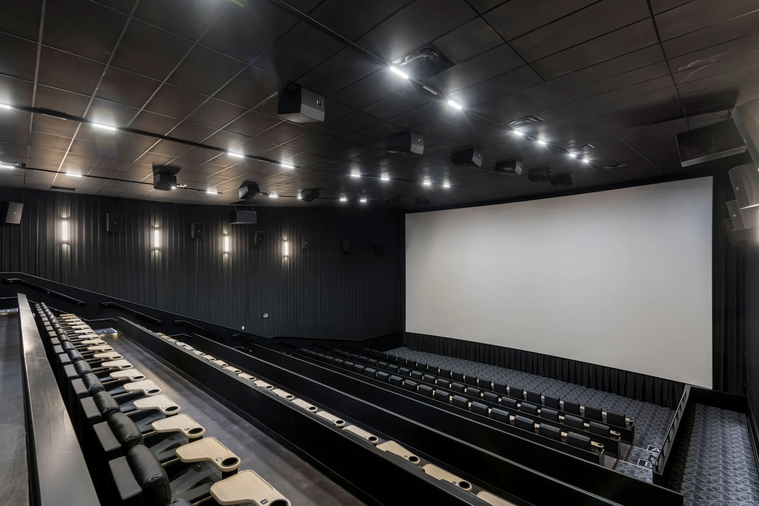 Empty modern movie theater with large screen, black walls, and tiered seating.