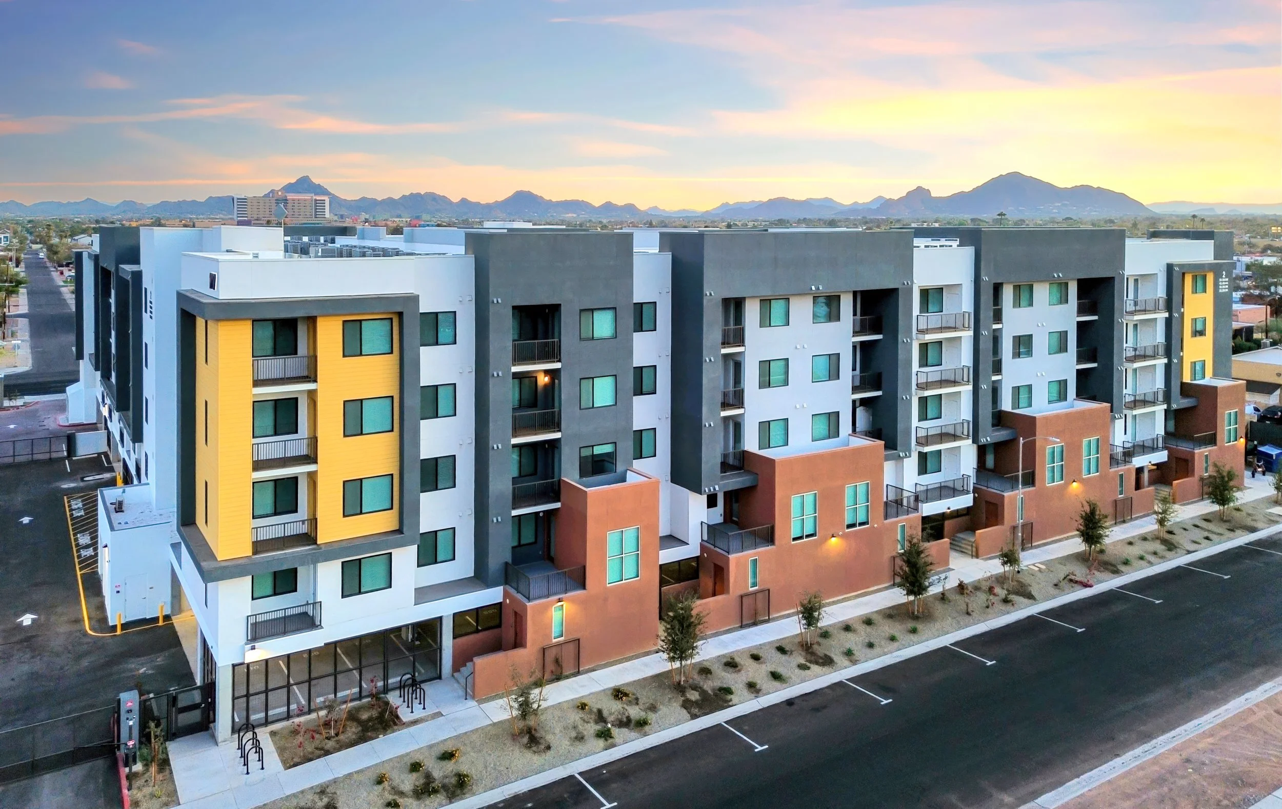 Modern multi-story apartment building with colorful facade and mountain background at sunset.