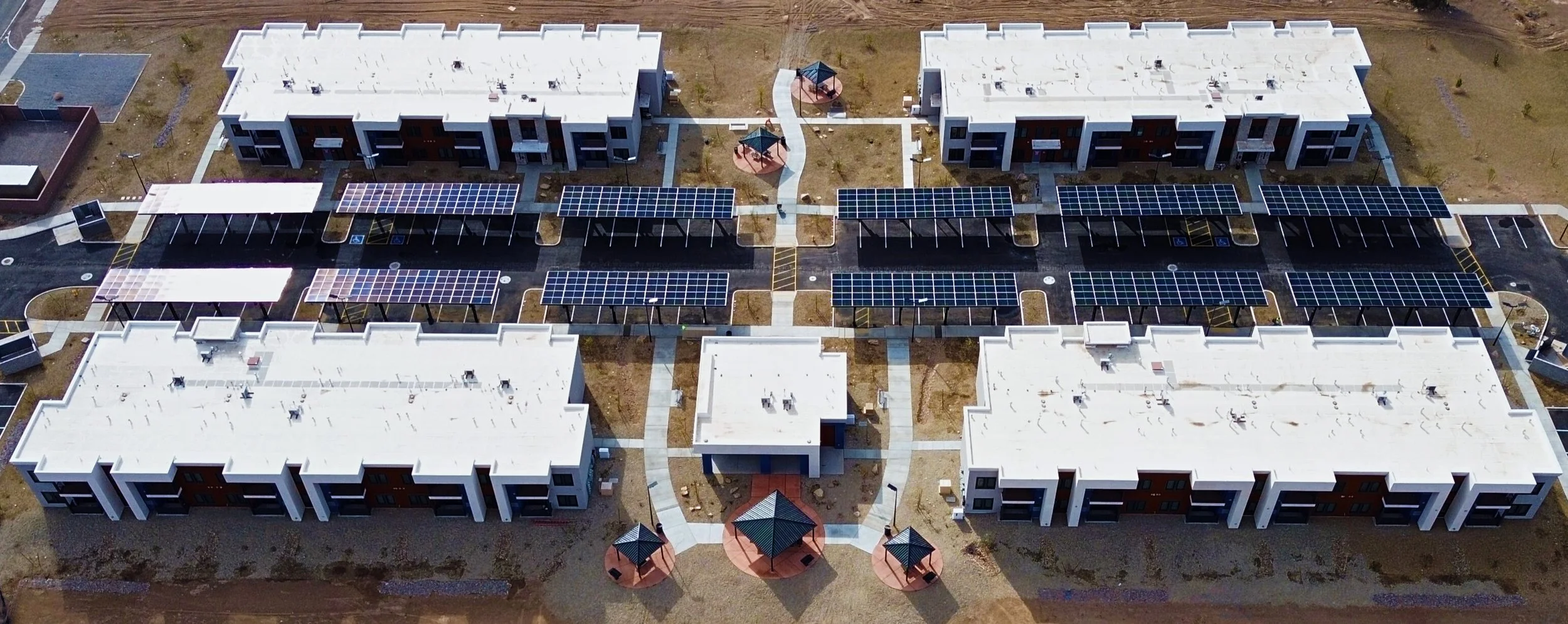 Aerial view of a modern apartment complex with multiple buildings, outdoor pathways, and solar panels on the roofs of some structures.