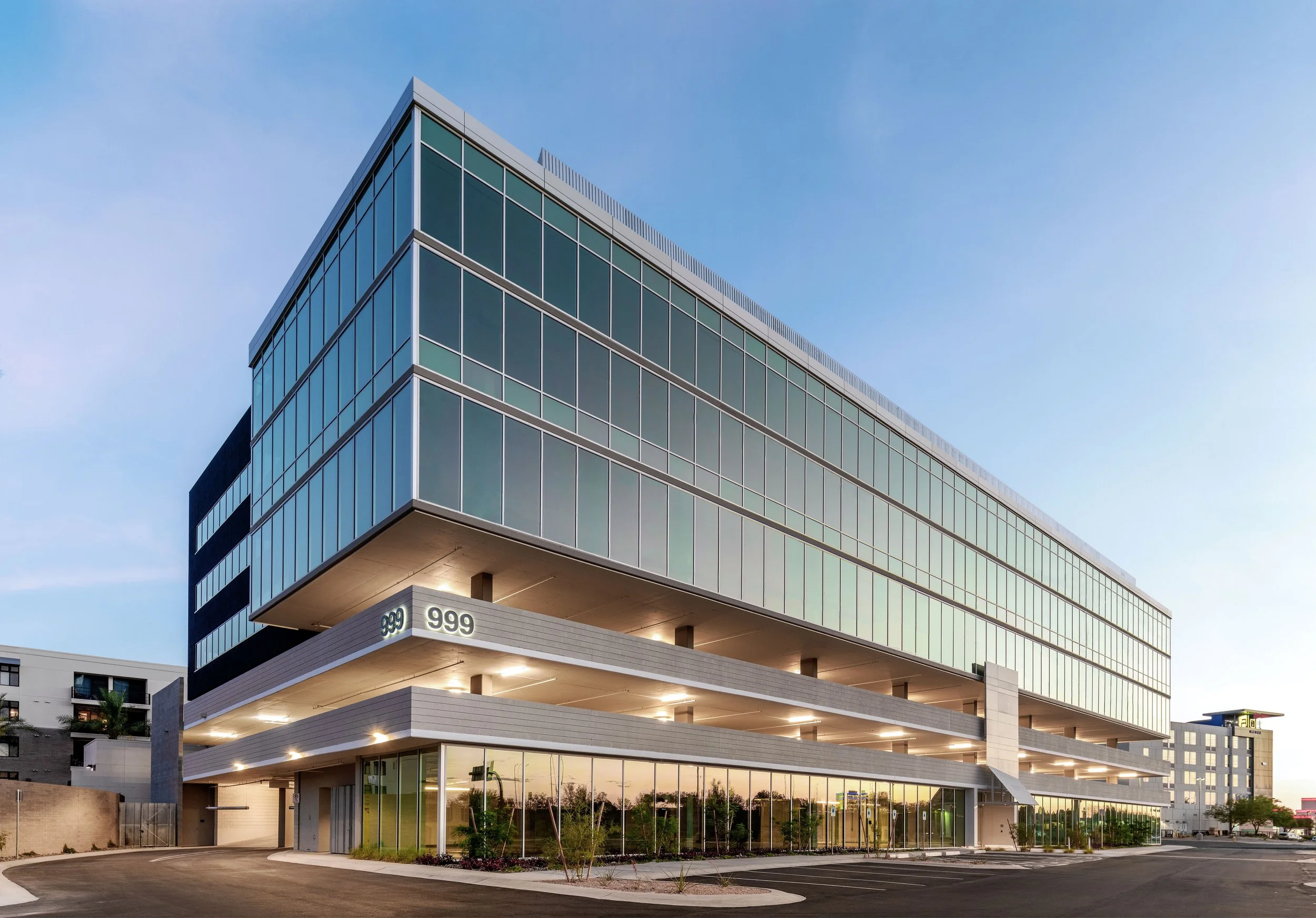 Modern multi-story office building with glass facade and parking lot, numbered 999, at dusk.