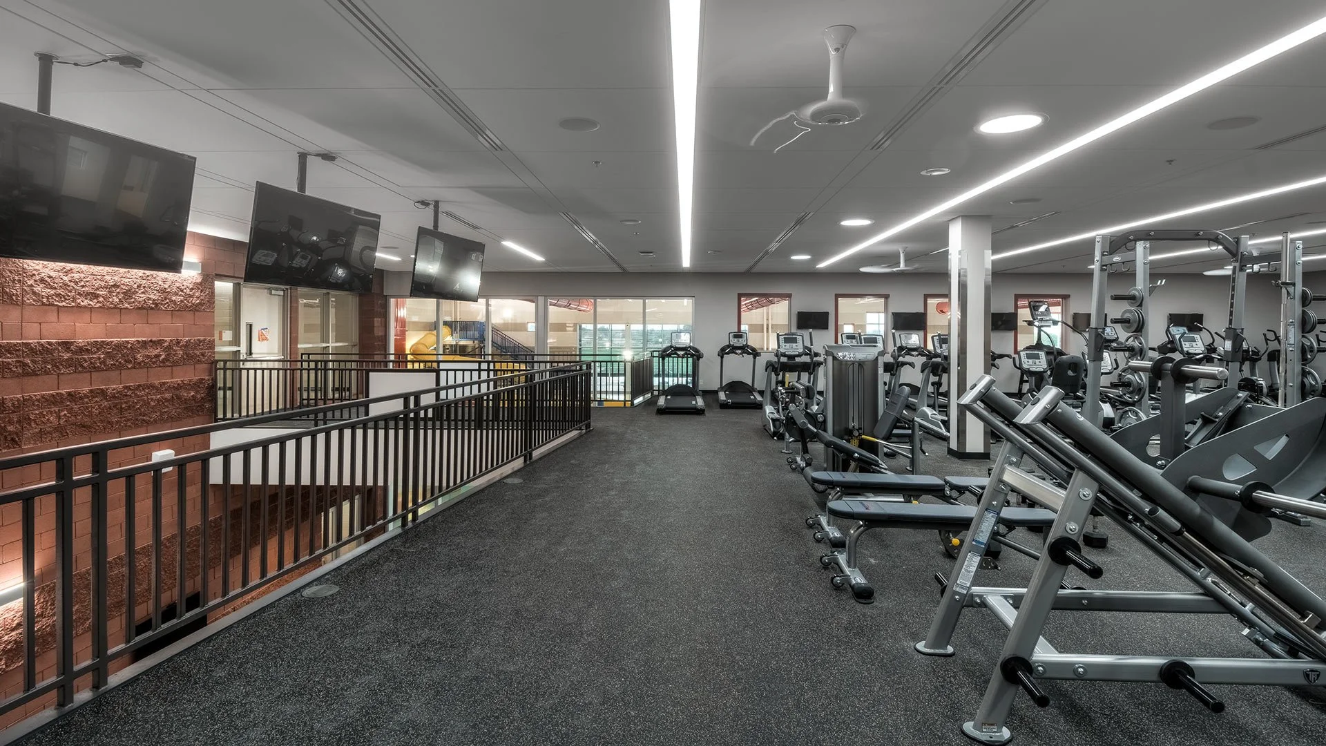 Empty gym with exercise equipment, treadmills, weights, and TVs on the wall.