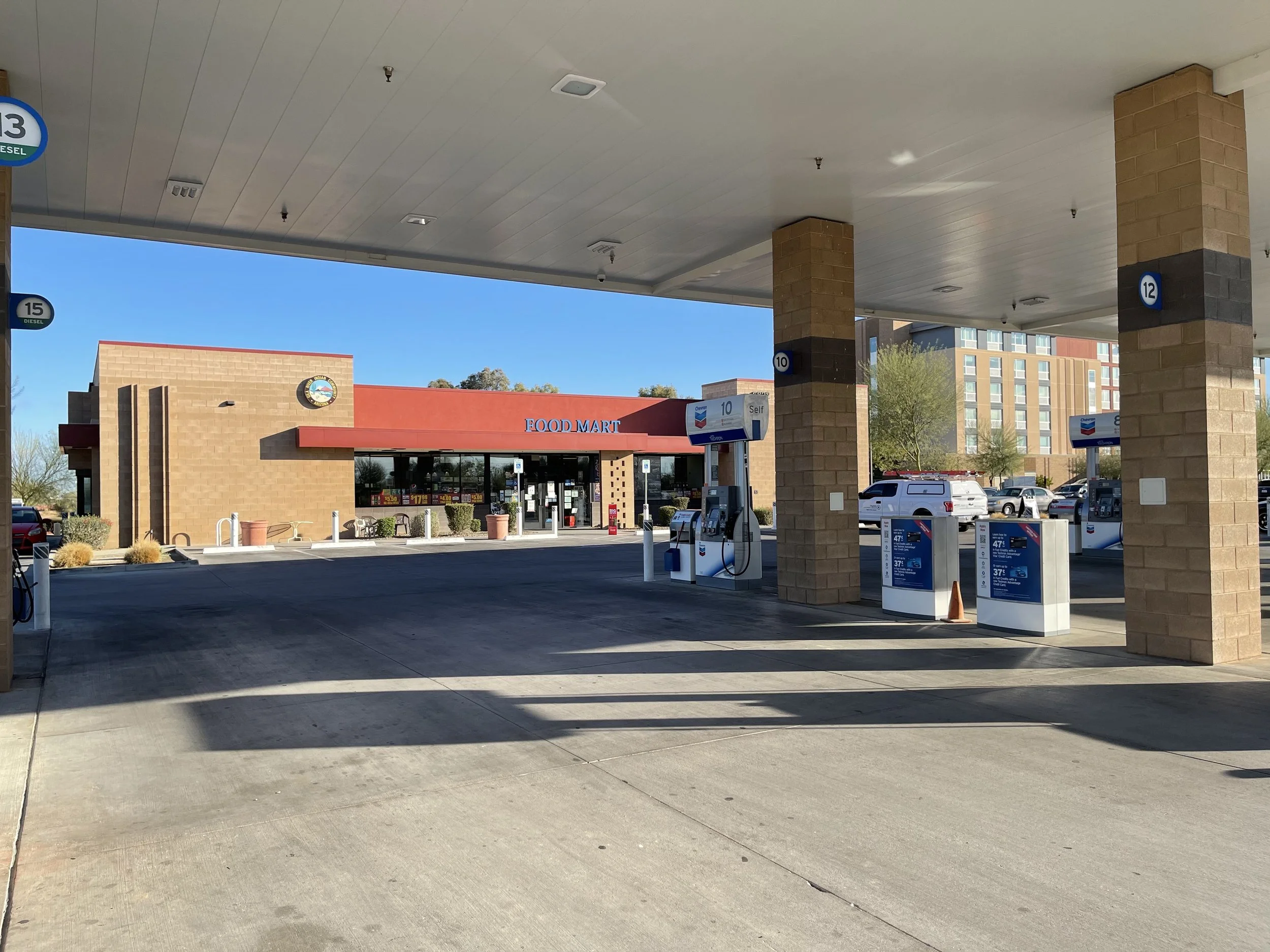 Empty gas station with fuel pumps and a convenience store in the background, under a clear blue sky.