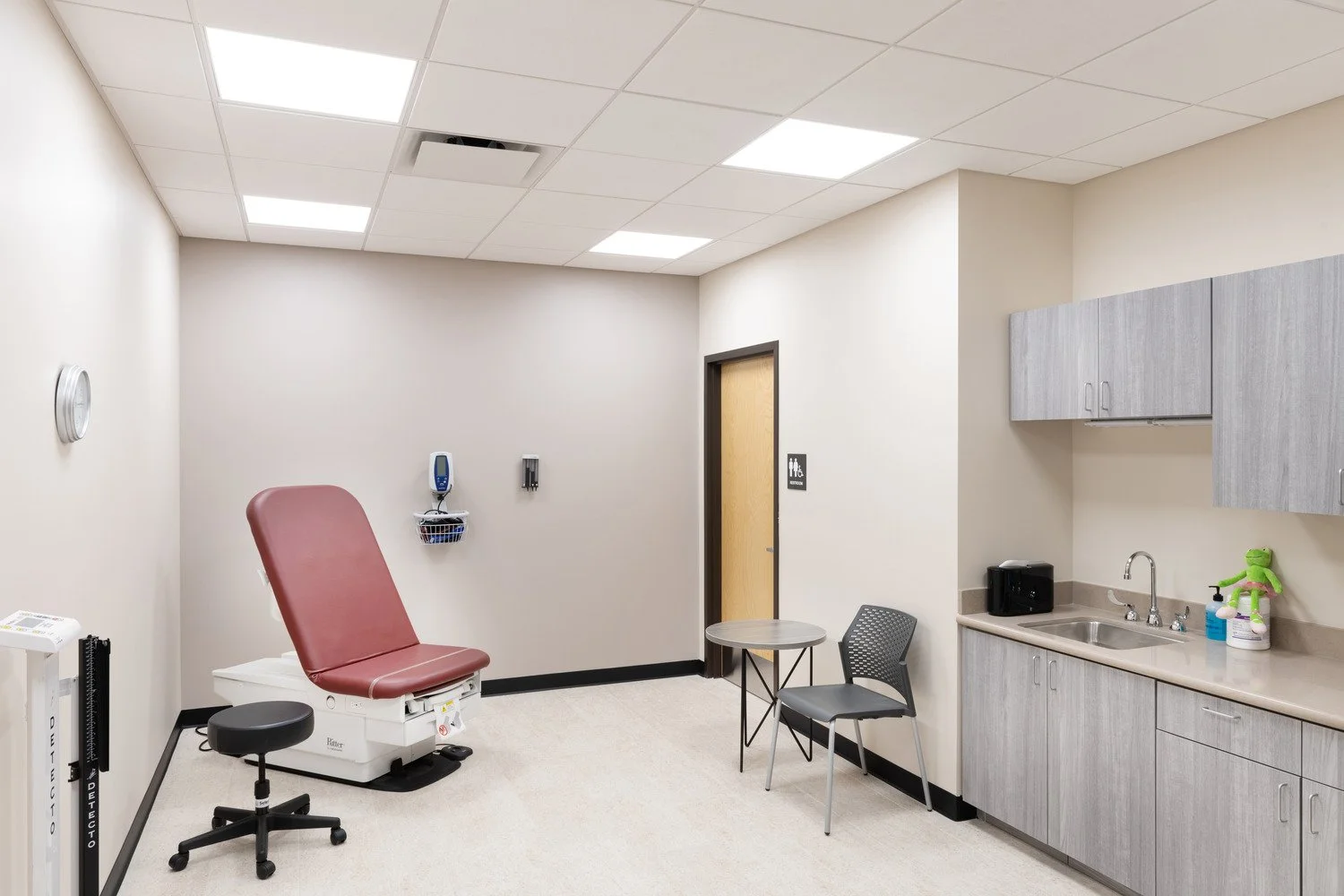 Hospital examination room with a medical chair, wall clock, sink, cabinets, and some medical supplies.