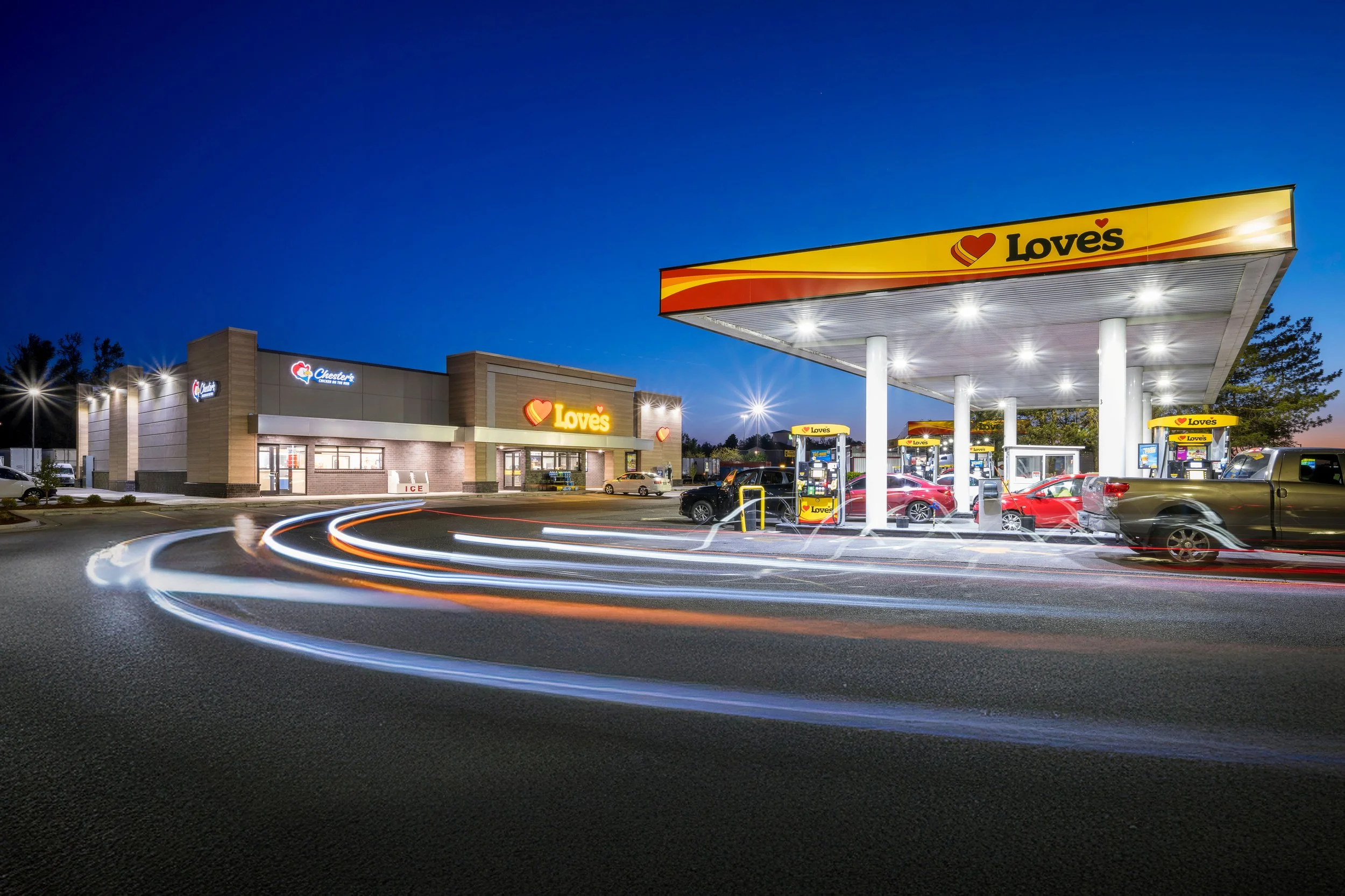 A Love's gas station and convenience store during twilight, with light trails from moving vehicles in the foreground.