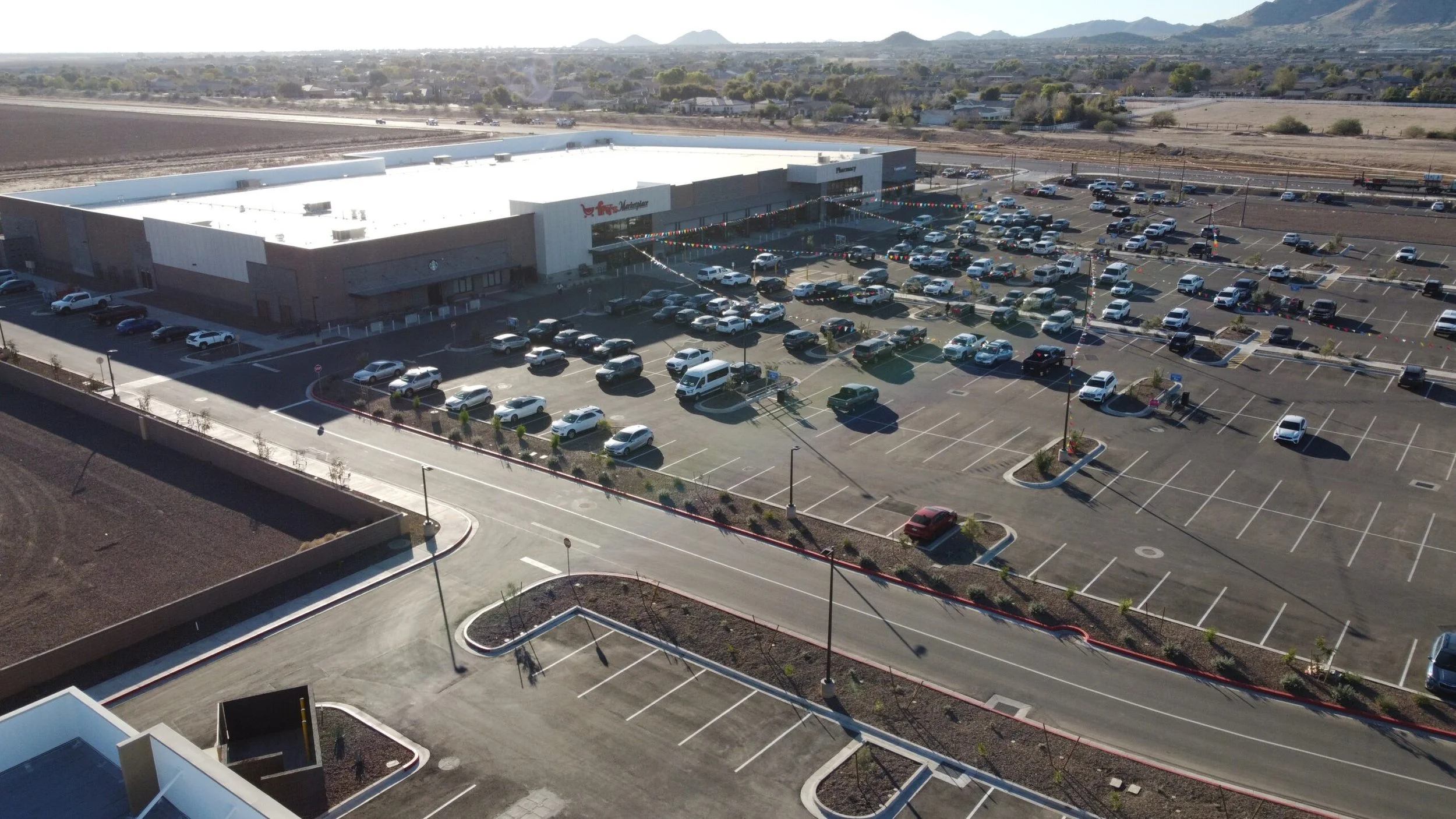 A large supermarket with a parking lot filled with cars, located in a semi-arid area with distant mountains in the background.